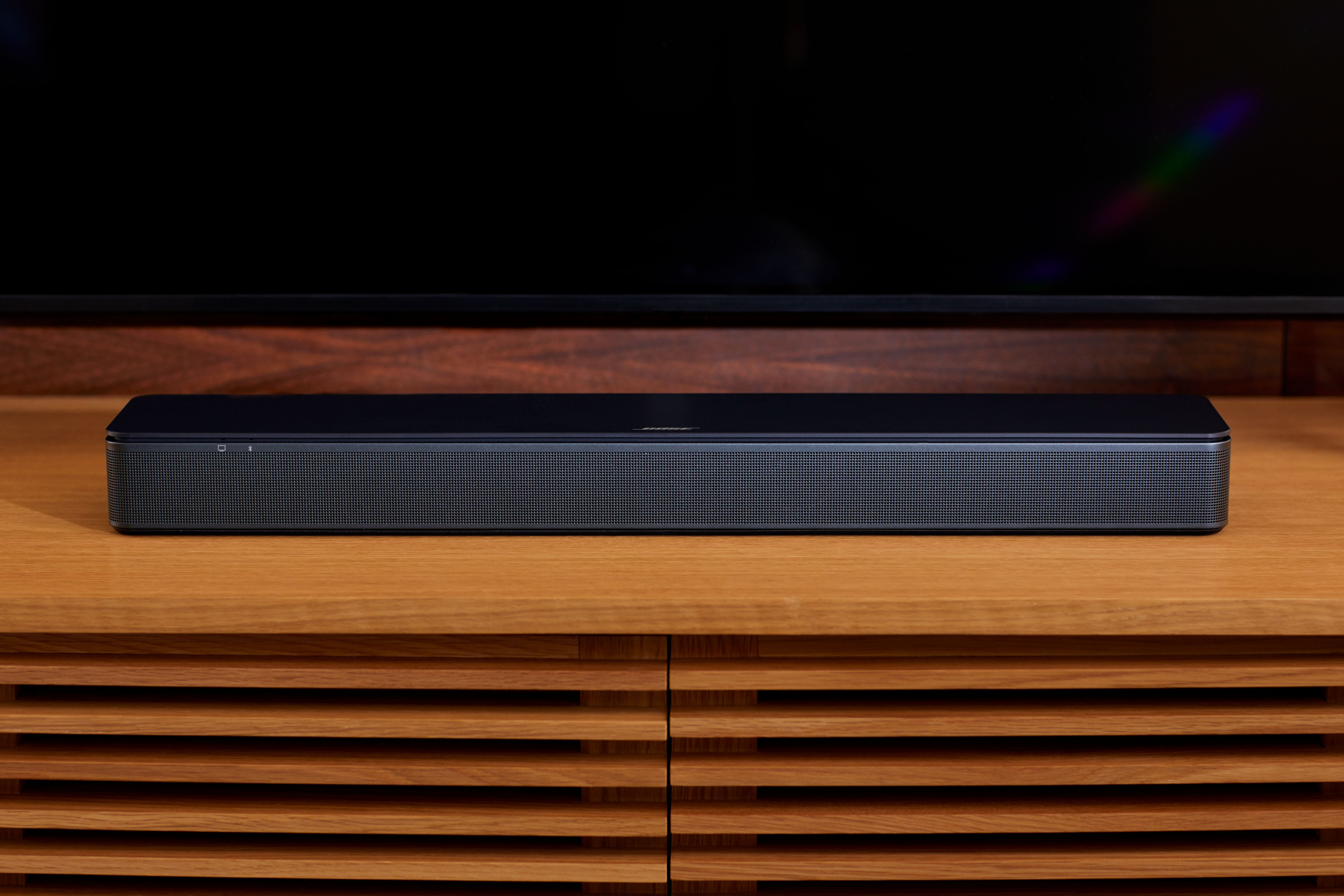 Schwarze Bose Soundbar auf Holzschrank, unter schwarzem TV-Bildschirm. Gut beleuchtet.