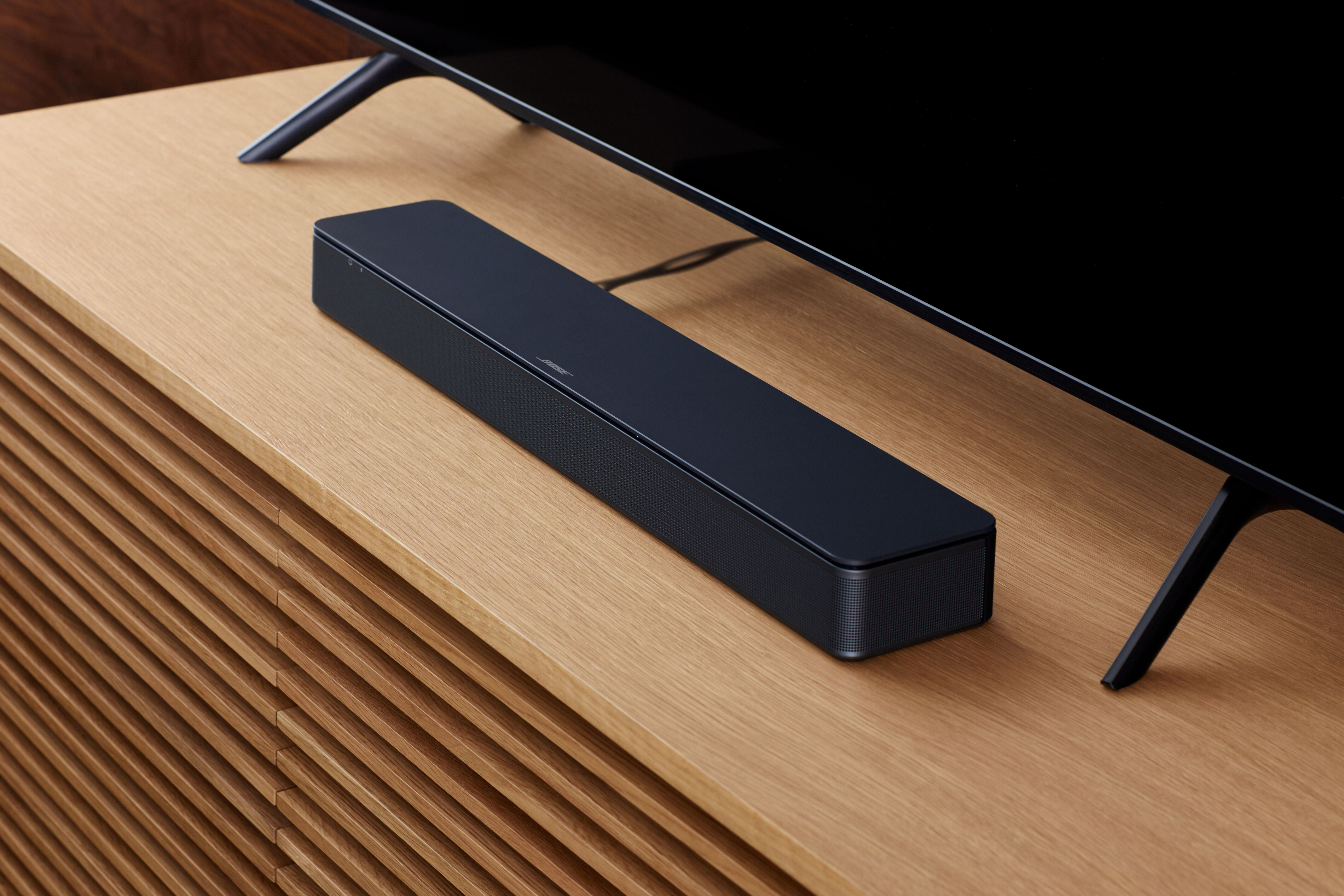 Eine Bose Soundbar auf einem Holzschrank vor einem schwarzen Fernseher.