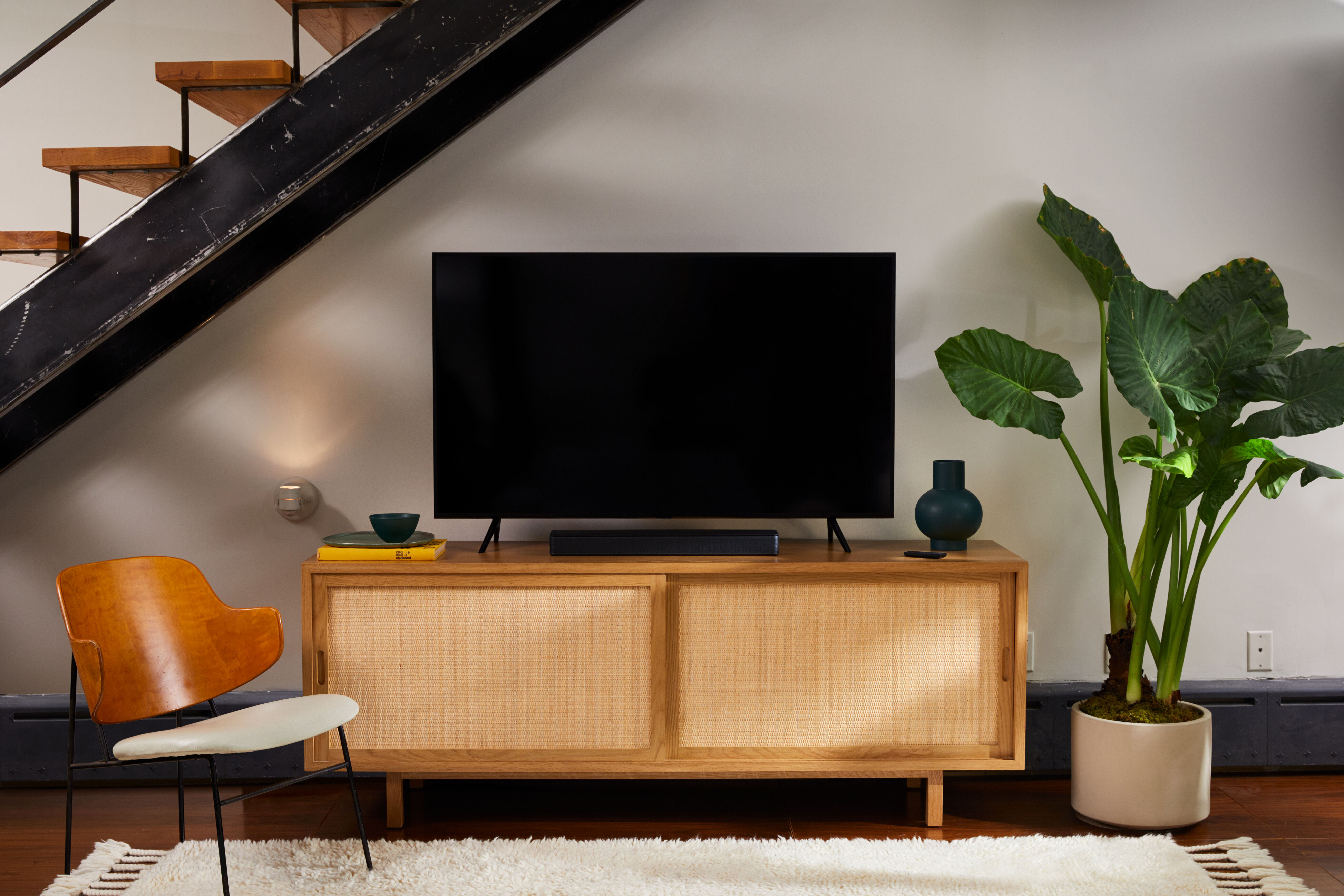 Wohnzimmer mit Fernseher, Schrank, Pflanze, Treppe und Teppich.