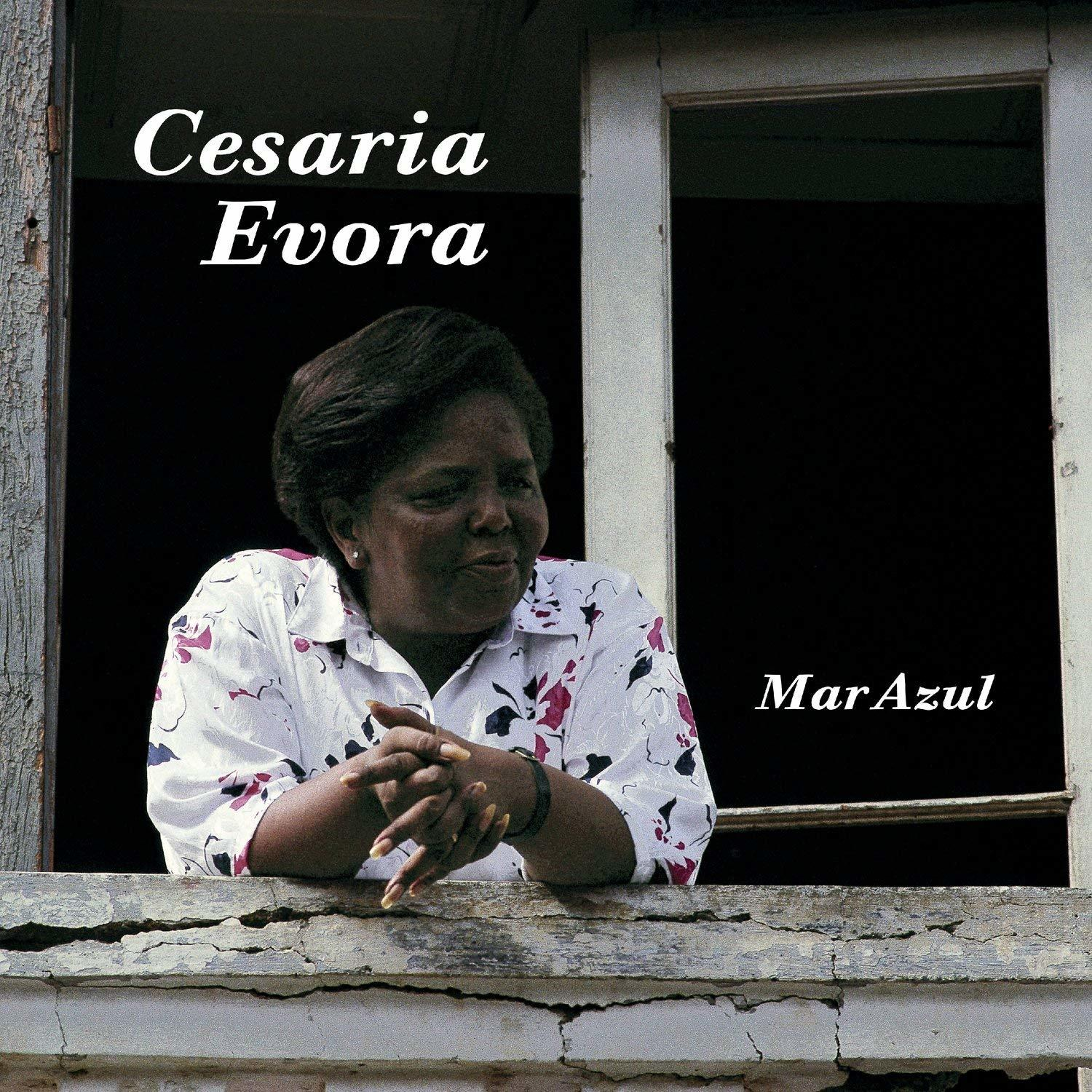 Cesaria Evora kinéz egy ablakon. Fehér virágos inget visel. A "Mar Azul" szavak jobbra láthatók.