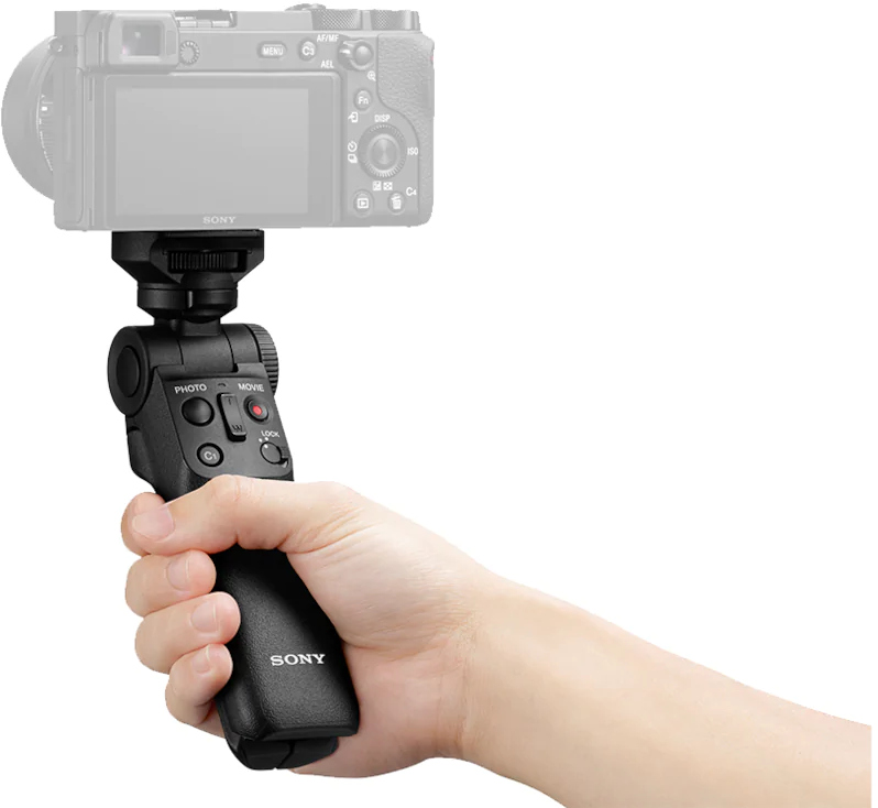 A hand holds a black Sony camera grip with controls.