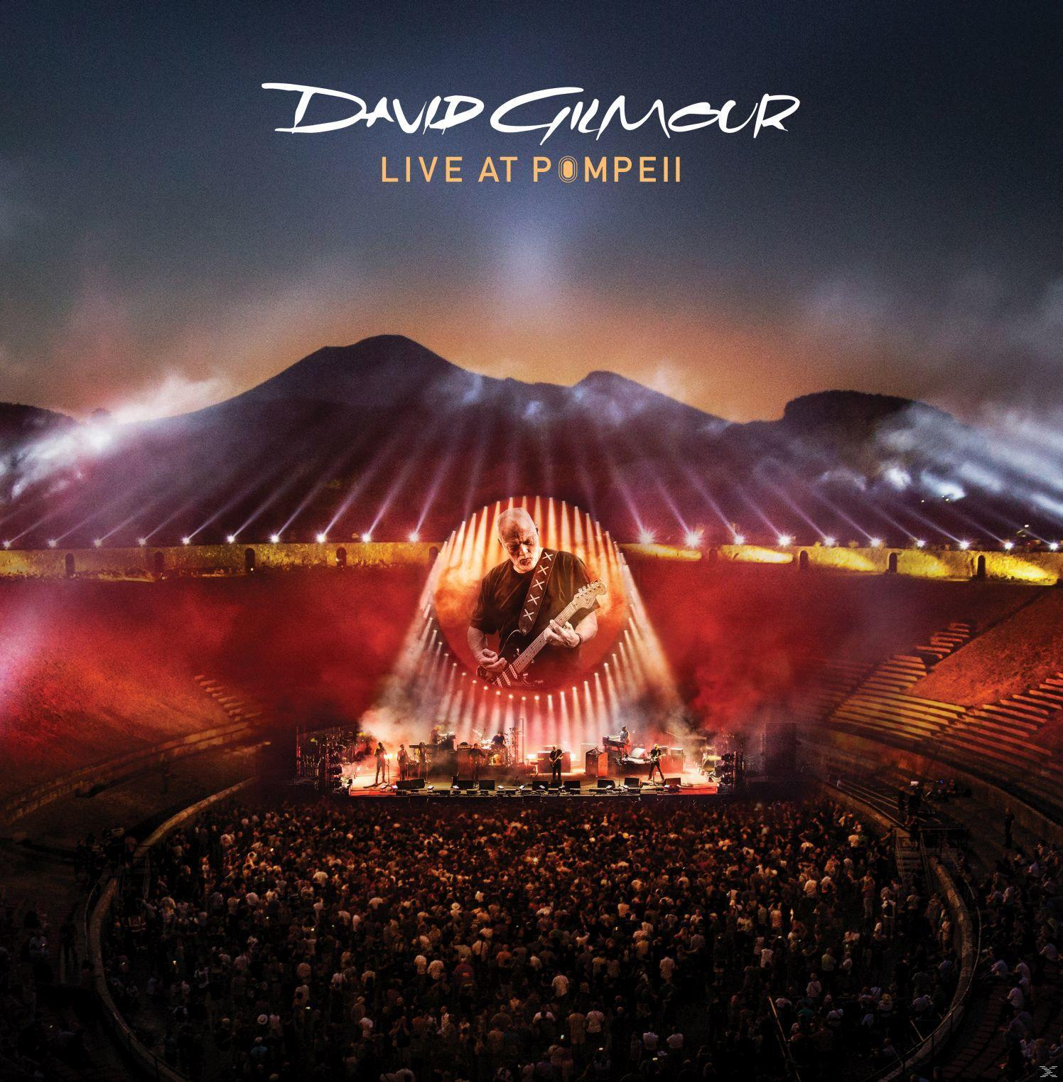 David Gilmour live in Pompeji. Bühnenlichter beleuchten eine Menschenmenge und eine Bergkulisse.