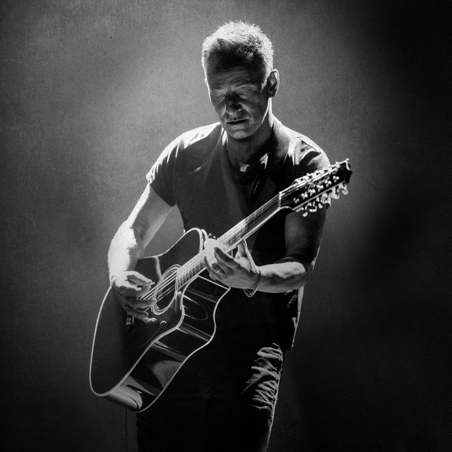 Bruce Springsteen spielt Gitarre, Schwarzweißfoto, dunkler Hintergrund.