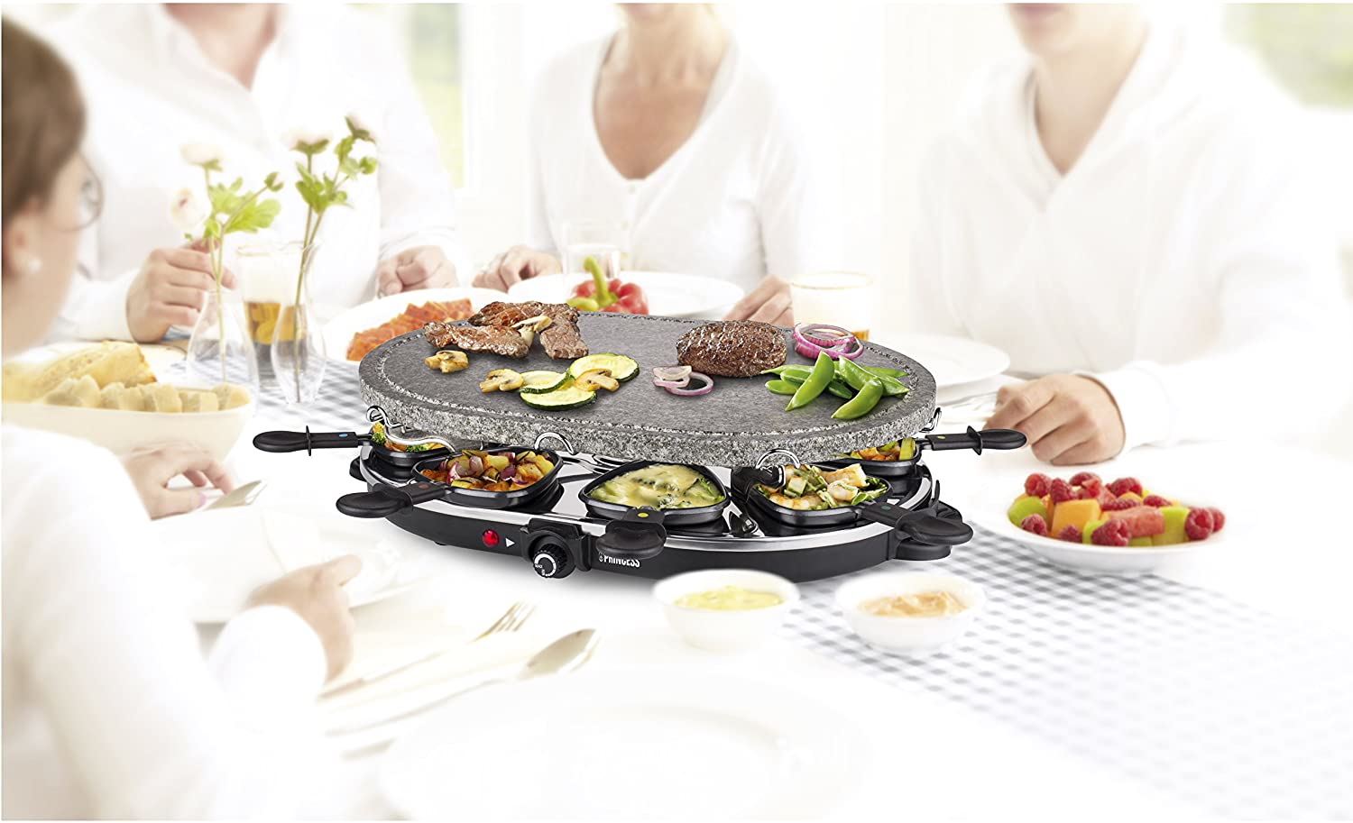 Raclette grill asztalon étellel és emberekkel. Zöldségek és hús a grillen.