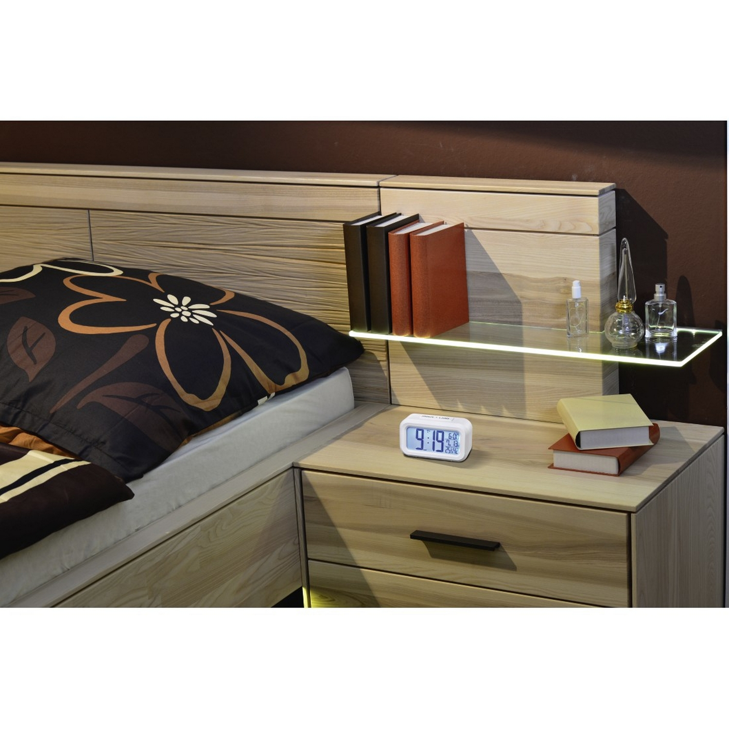 Una mesita de noche en el dormitorio con un reloj digital, libros y adornos.