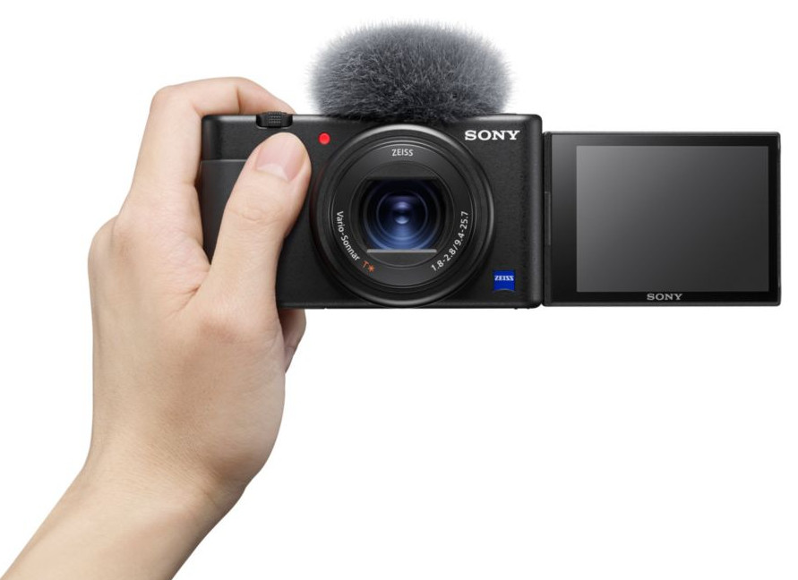 Een persoon die een zwarte camera vasthoudt met een microfoon erop en een open scherm.