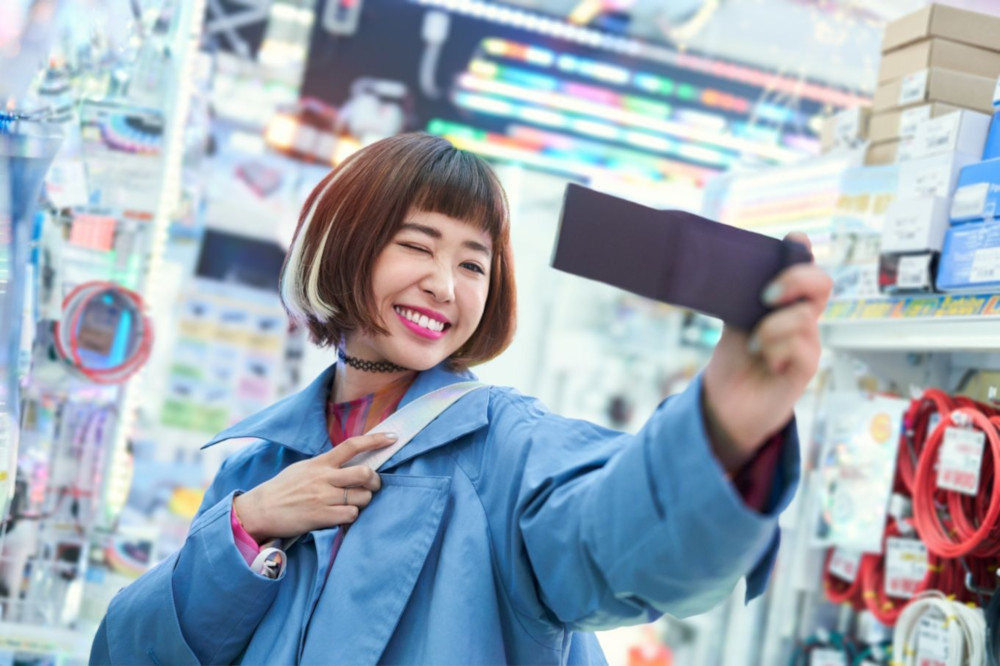 Een vrouw in een blauwe jas die een selfie maakt in een winkel, glimlachend.