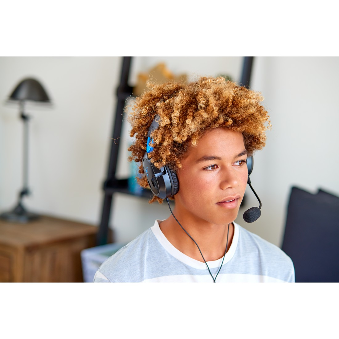 Ein junger Mensch mit lockigem Haar trägt ein Headset und blickt nach rechts. Hintergrund: ein Raum.