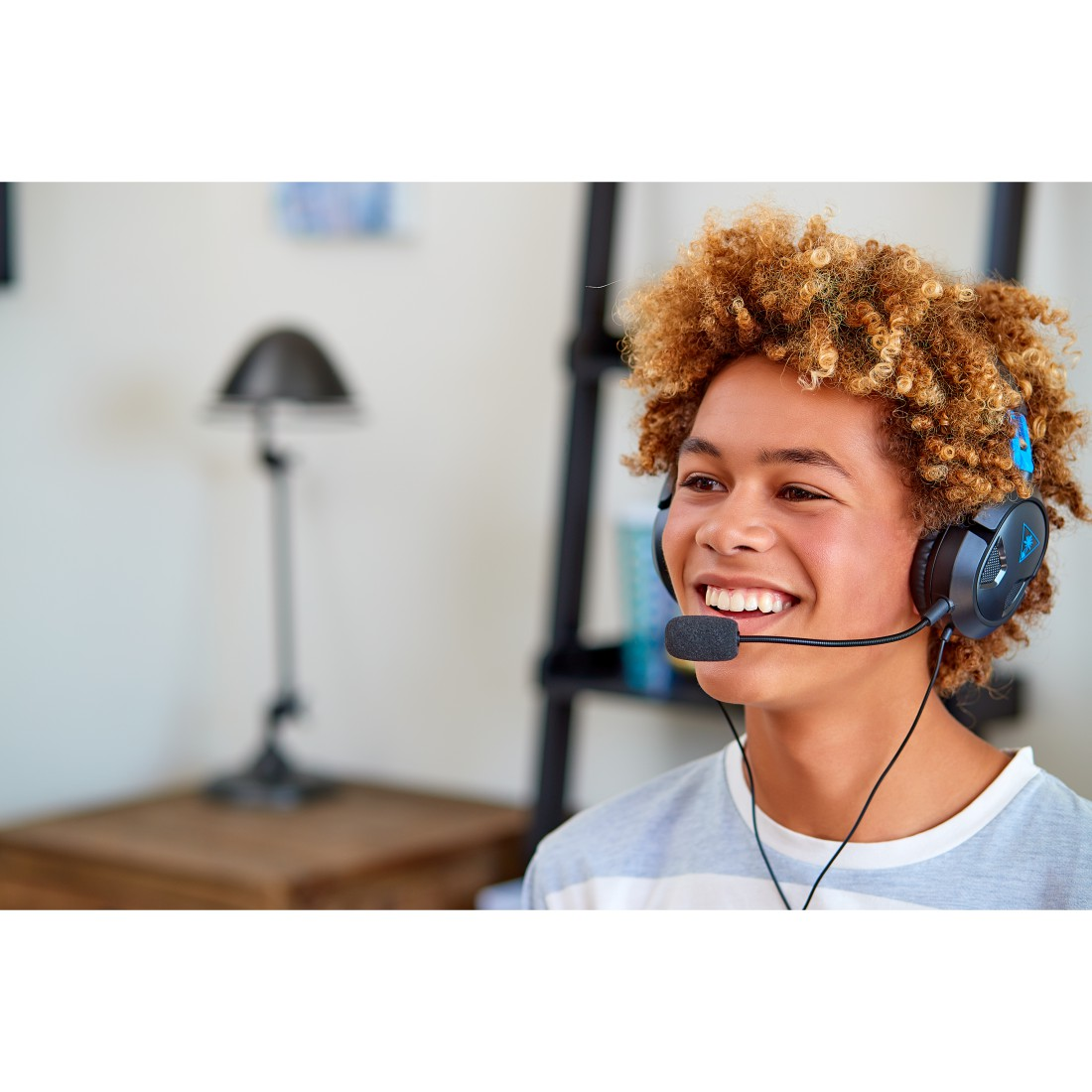 Lachender Junge mit lockigem Haar, der ein Gaming-Headset mit Mikrofon trägt.