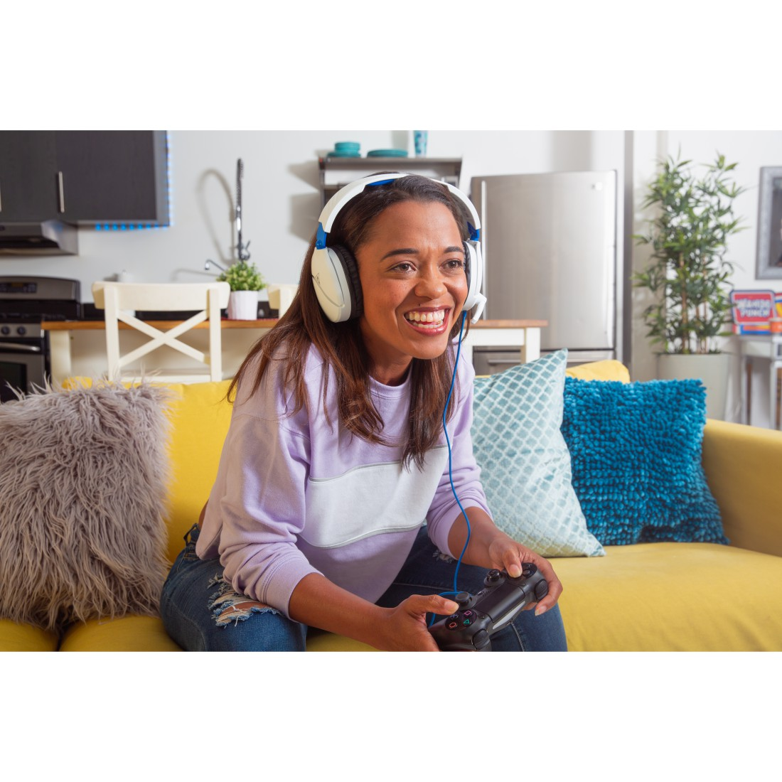 Frau spielt Spiel mit Controller und Kopfhörern auf gelbem Sofa, lächelnd.