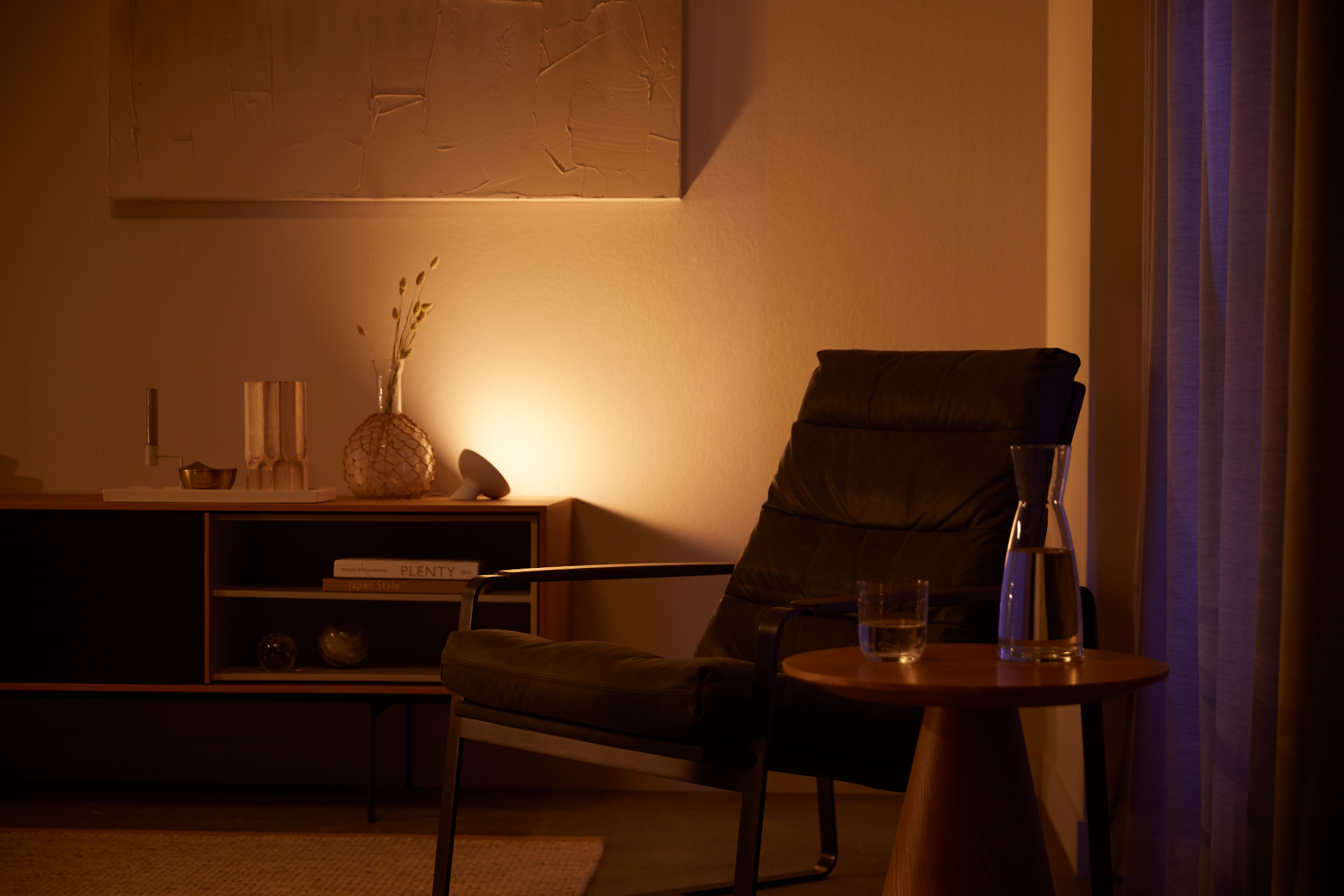 Wohnzimmer mit Stuhl, Tisch mit Glas und Schrank. Warme Beleuchtung.