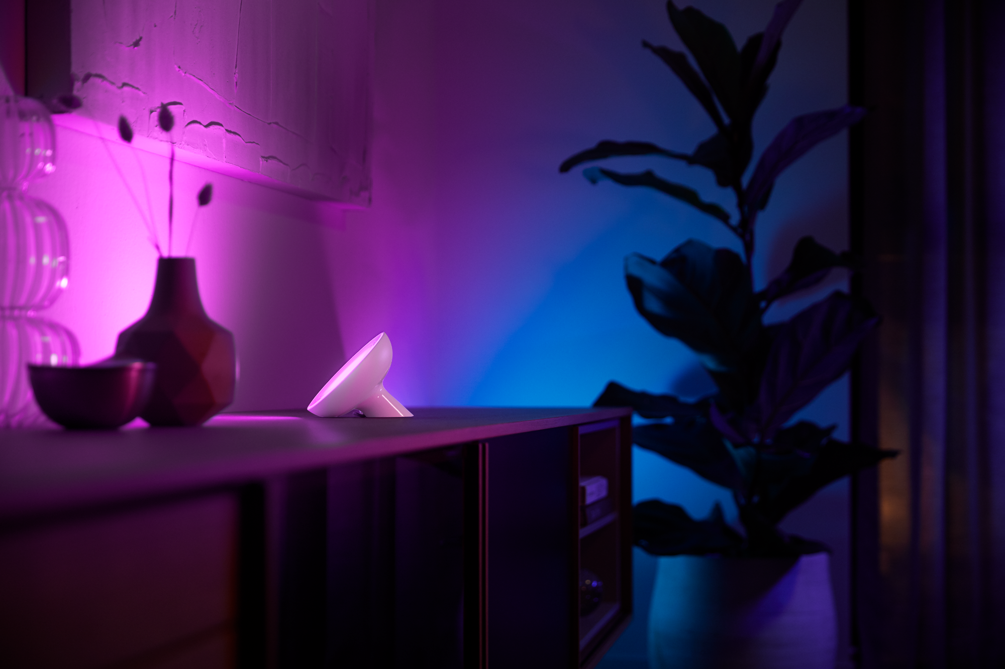 Moderne Smart-Lampe auf dunkler Oberfläche mit lila und blauer Umgebungsbeleuchtung.