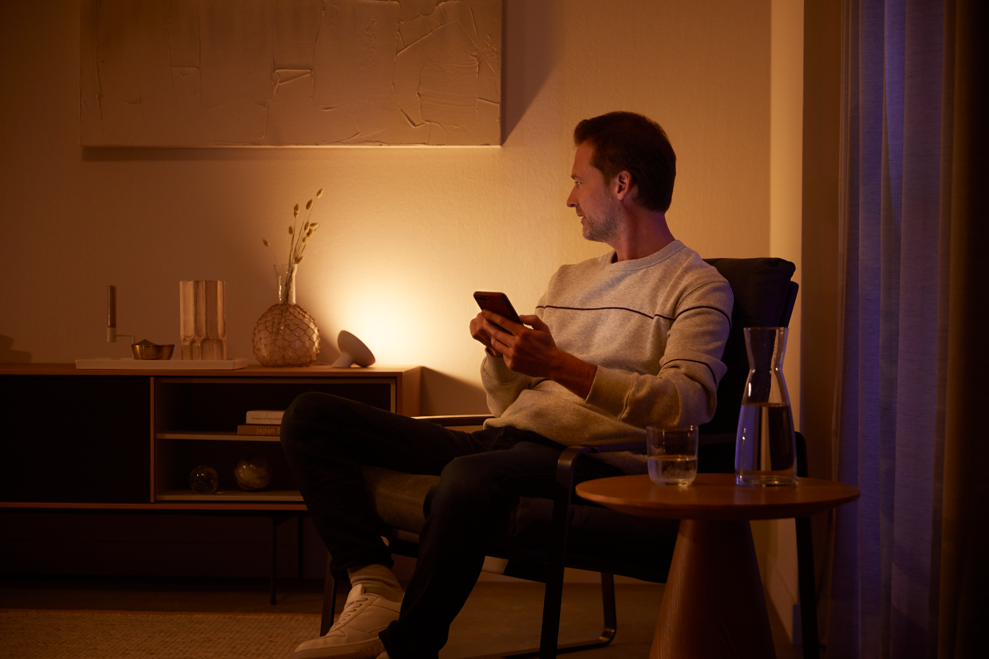 Mann mit Smartphone sitzt in einem beleuchteten Raum.