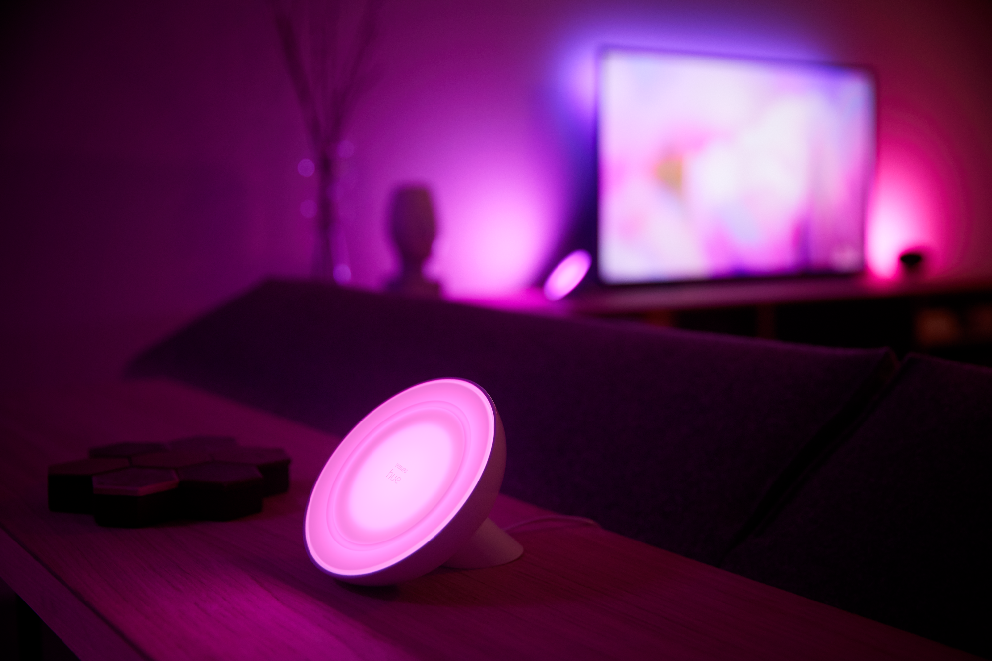 Weiße und rosa Smart-Lampe auf einem Tisch, mit einem Fernseher im Hintergrund.