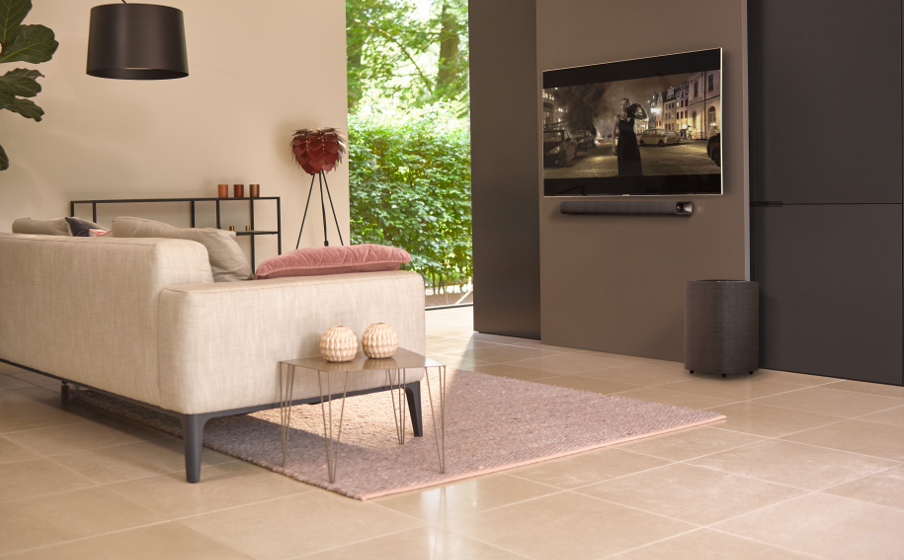 Woonkamer met bank, tafel, tv en soundbar en een kleed.