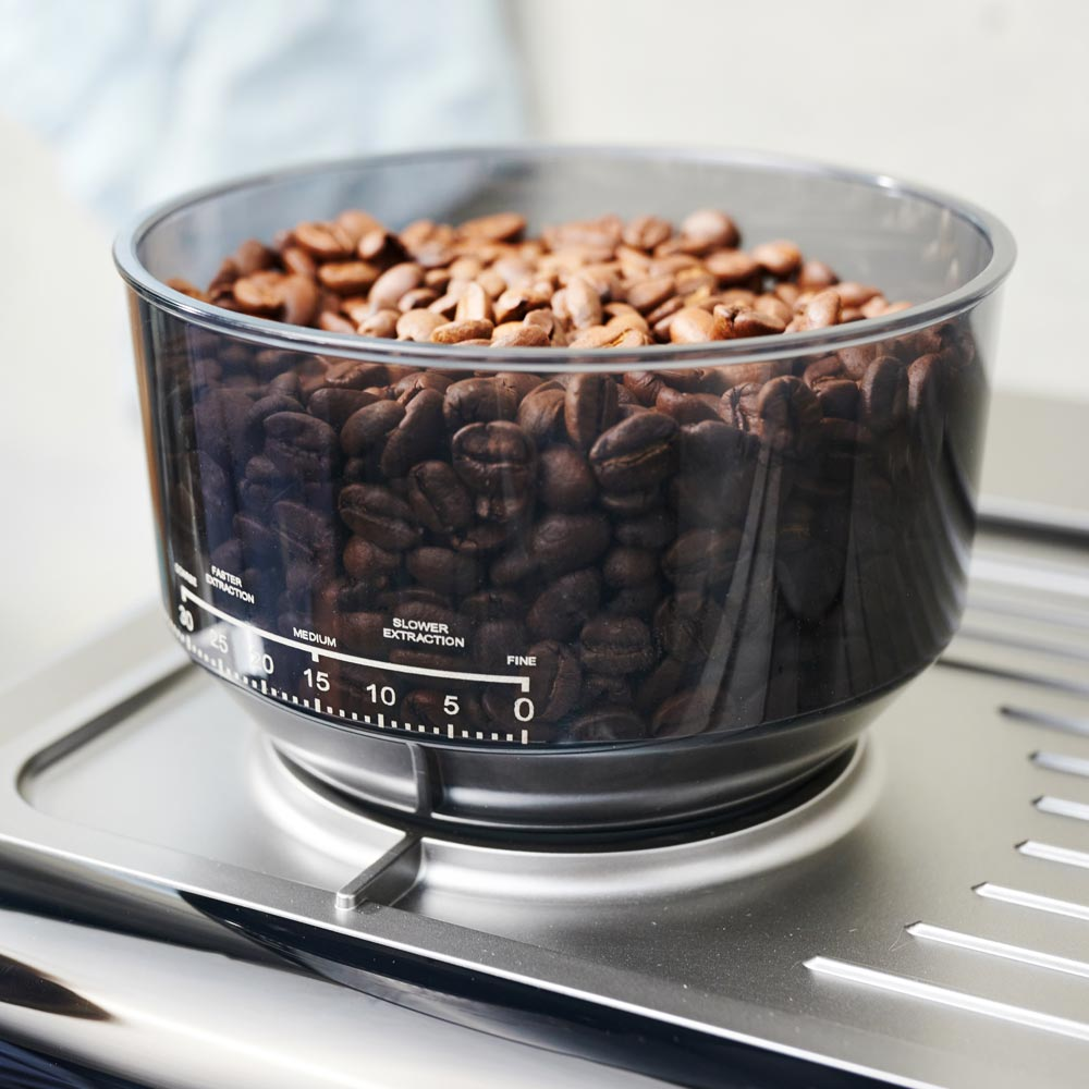 Ein transparenter Behälter mit Kaffeebohnen steht auf einer silbernen Oberfläche.