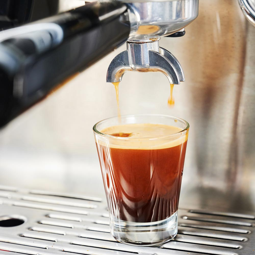 Kaffee fließt aus einer Maschine in ein Glas und erzeugt einen reichhaltigen, dunklen Espresso.