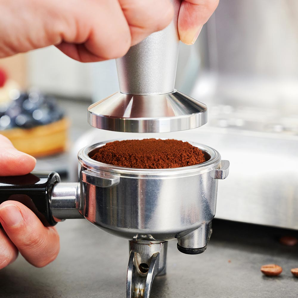 Person drückt Kaffeepulver mit einem Tamper in einen Siebträger.