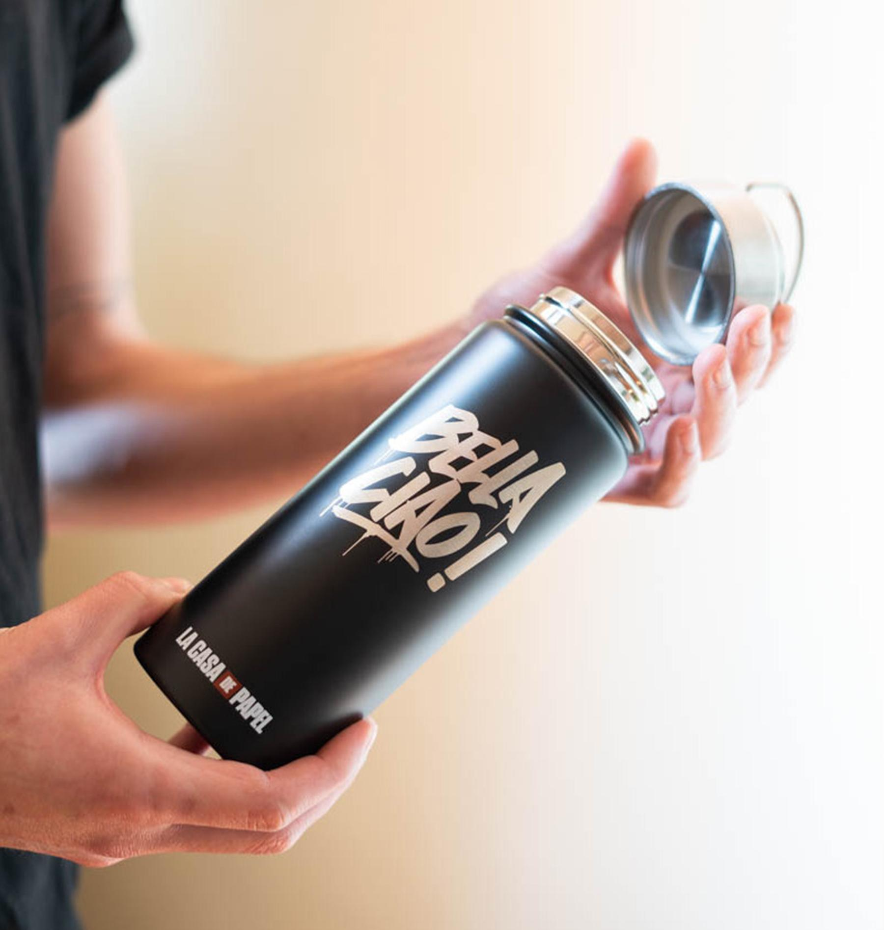Schwarze Flasche mit 'BELLA CIAO!'-Text, die gehalten wird. Weißer Hintergrund.