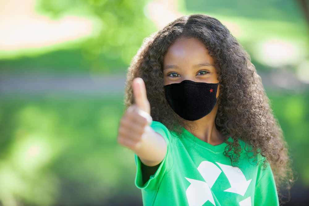 Jong meisje met een zwart masker met een rode ster, geeft een duim omhoog in de buitenlucht.