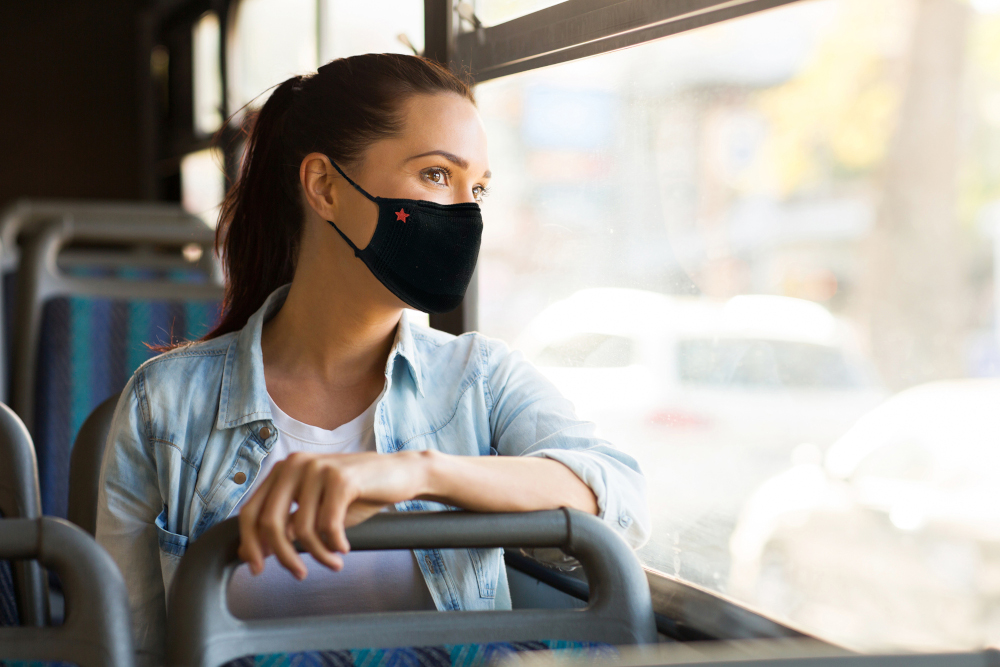 Vrouw in de bus met een zwart masker met een rode ster, kijkt uit het raam.