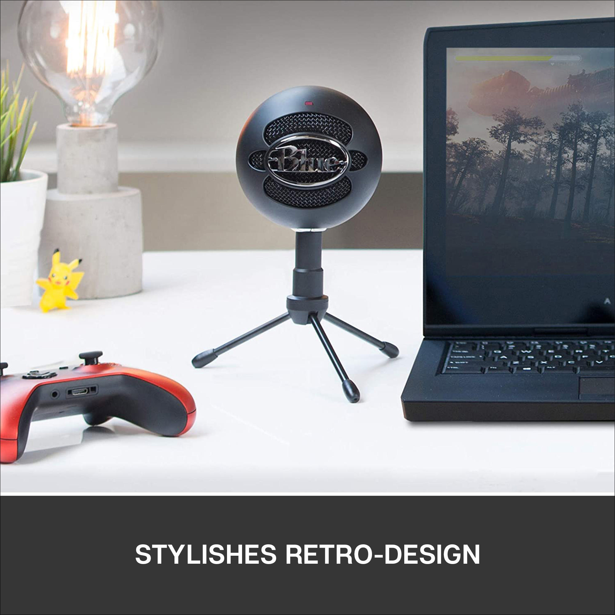 Ein schwarzes Blue Yeti Mikrofon auf einem Stativ, neben einem Laptop und einem Gamecontroller.