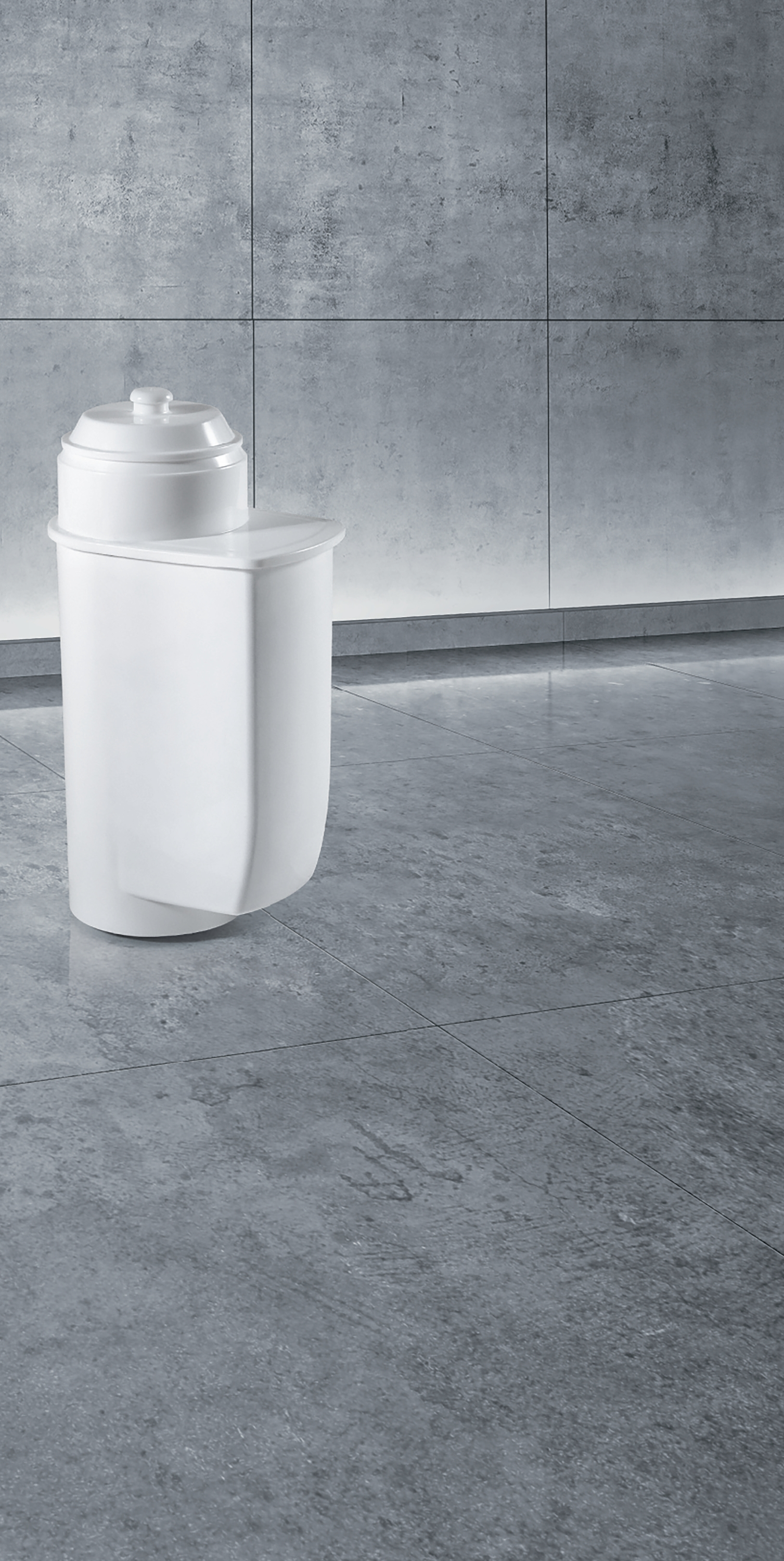 A white water filter on a gray tile floor, with a gray tiled wall.