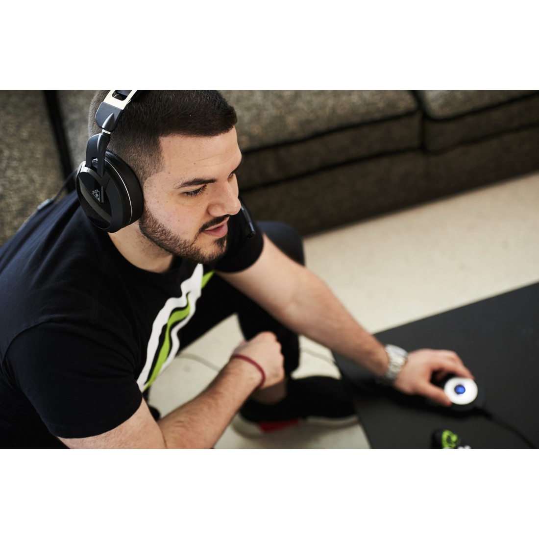 Mann mit Kopfhörern, blickt nach unten. Schwarzes T-Shirt, schwarzer Tisch, Gaming-Setup.