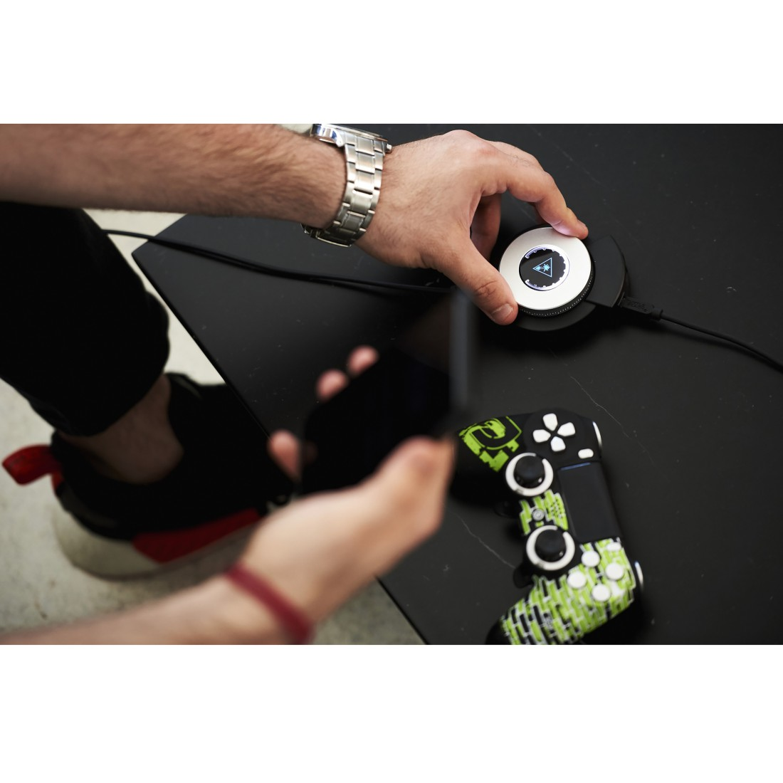 Hände, die mit einem Controller und einem Gaming-Gerät auf schwarzer Oberfläche interagieren.