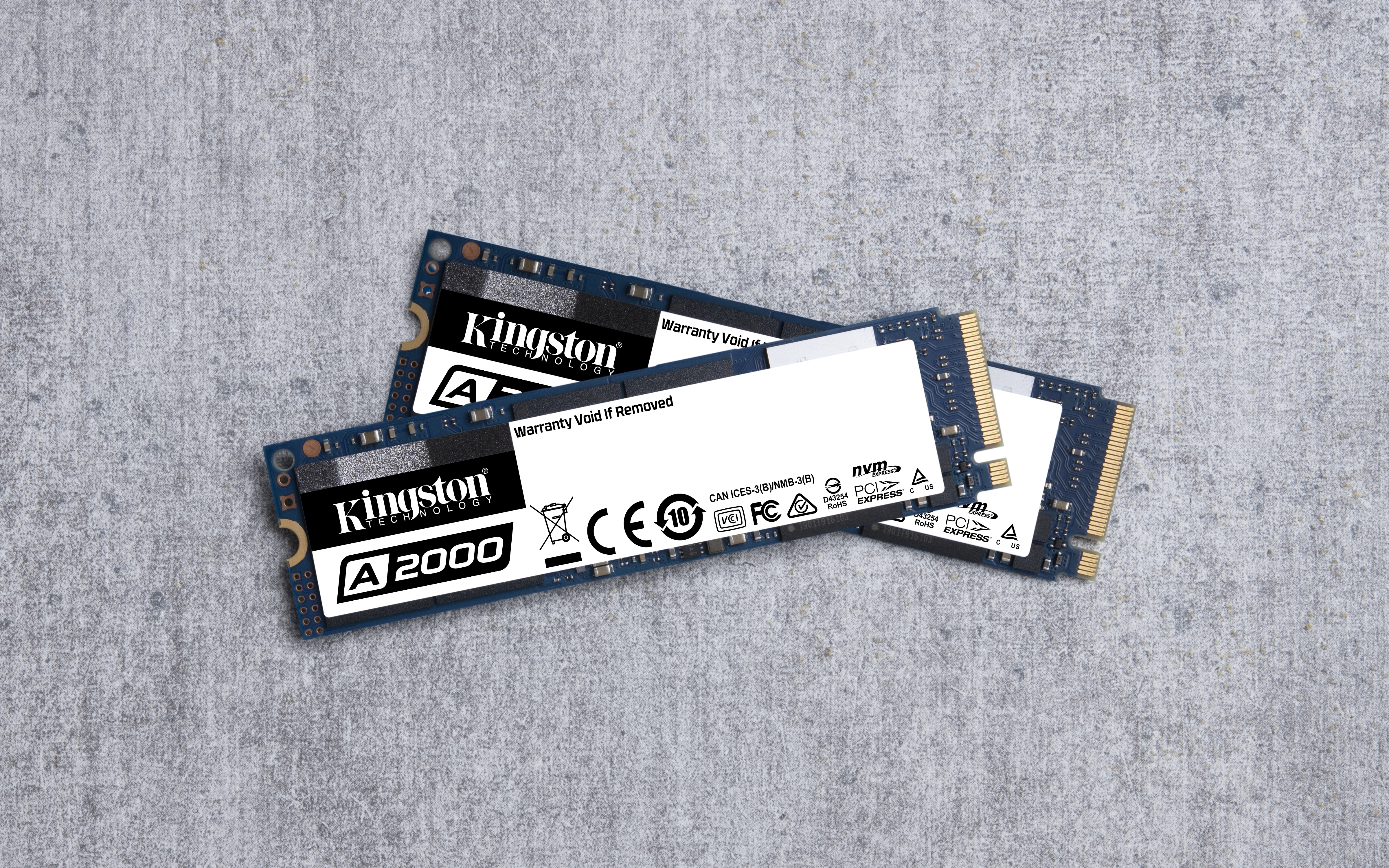 Drei Kingston A2000 SSDs auf grauer Oberfläche, jede mit weißem Etikett.