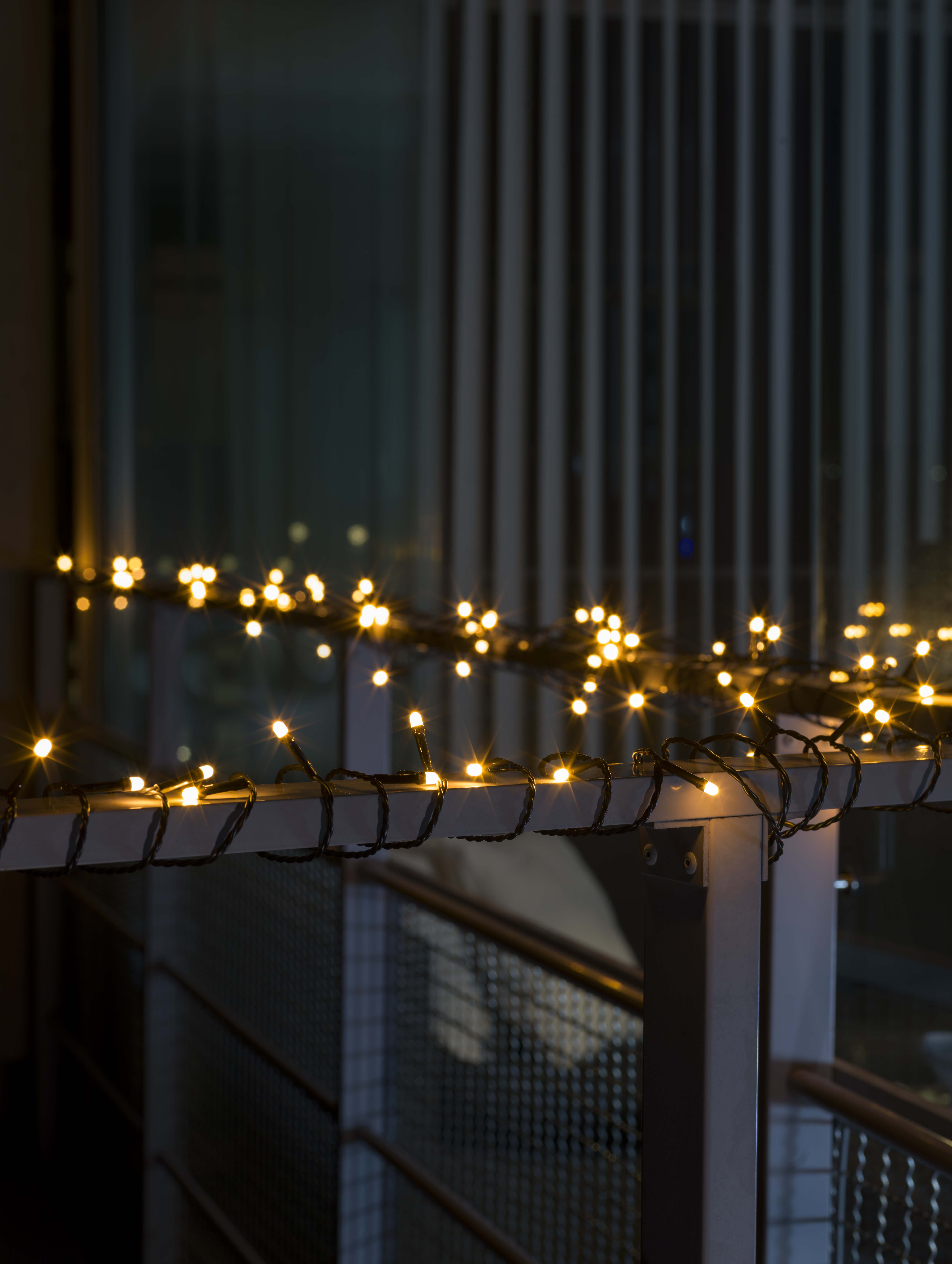 Lichterkette auf einem Metallgeländer. Die Lichter sind gelb und der Hintergrund ist dunkel.