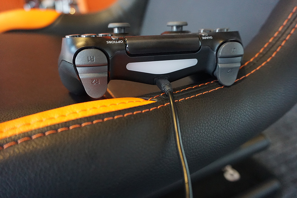Black PS4 controller on an orange and black gaming chair.