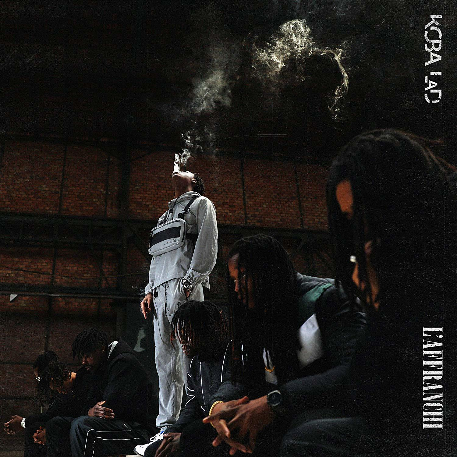 Man smoking, standing. Others seated. Background: brick wall, dark. Album cover.