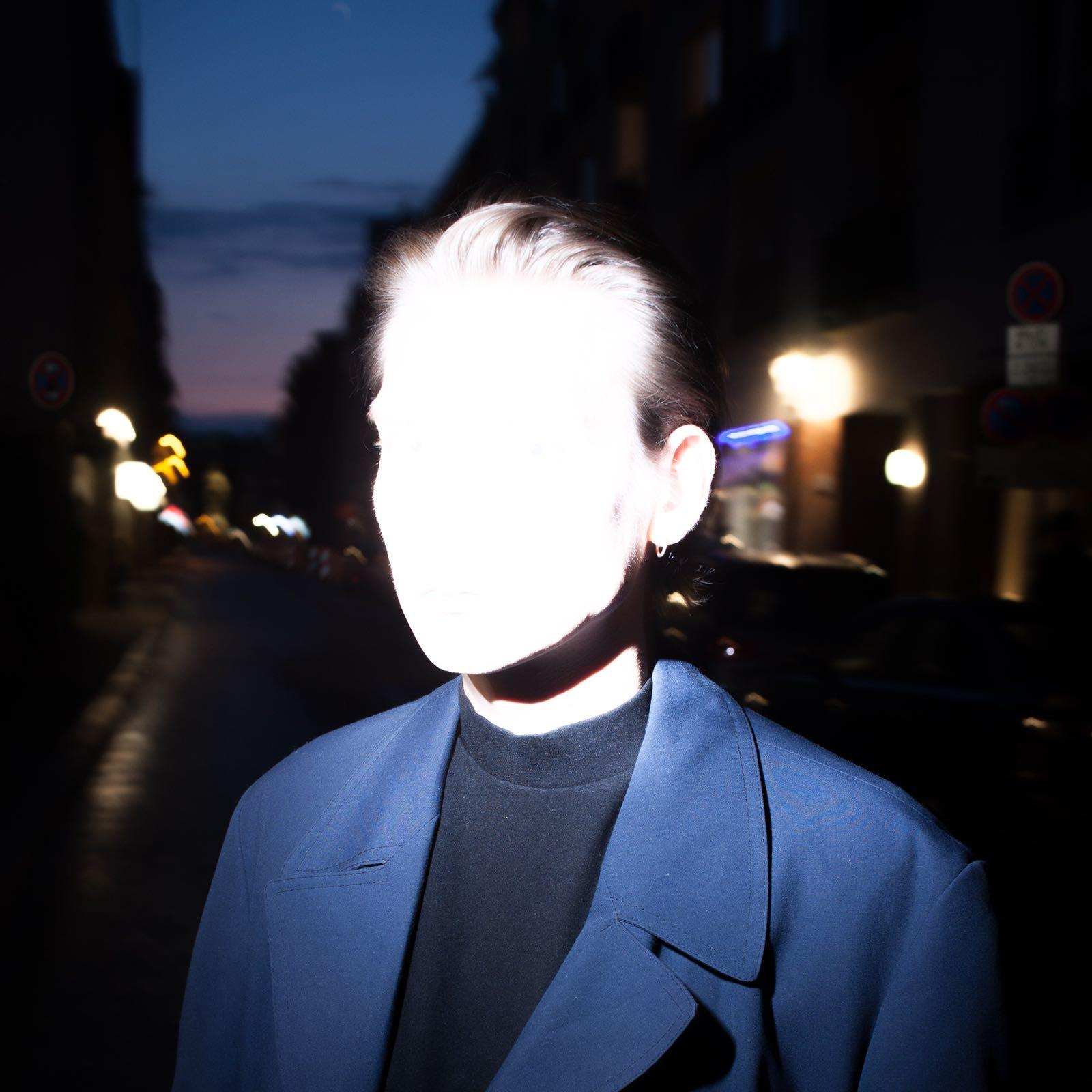 Person with light face in blue jacket at night on a street. Dark background.