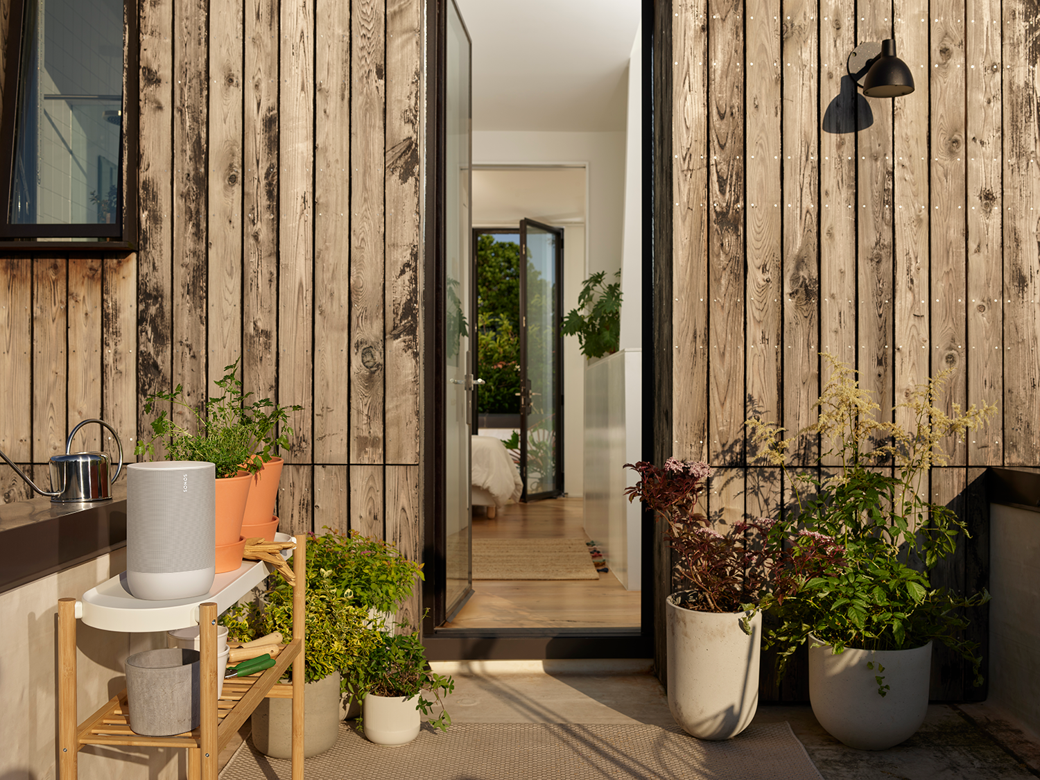 Buitenomgeving met een speaker, planten en open deur naar een slaapkamer.