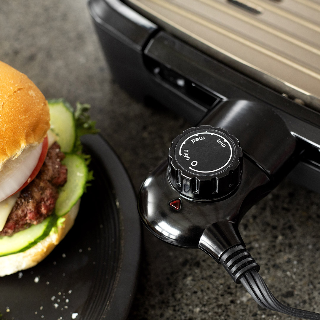 Egy hamburger és egy grillszabályozó tárcsa egy grill mellett.