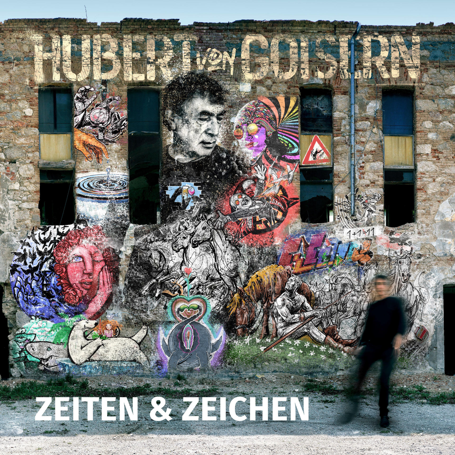 Ein Wandgemälde auf einer Backsteinmauer mit Graffiti und Bildern. Es enthält den Namen 'Hubert von Goisern' und den Titel 'Zeiten & Zeichen'.