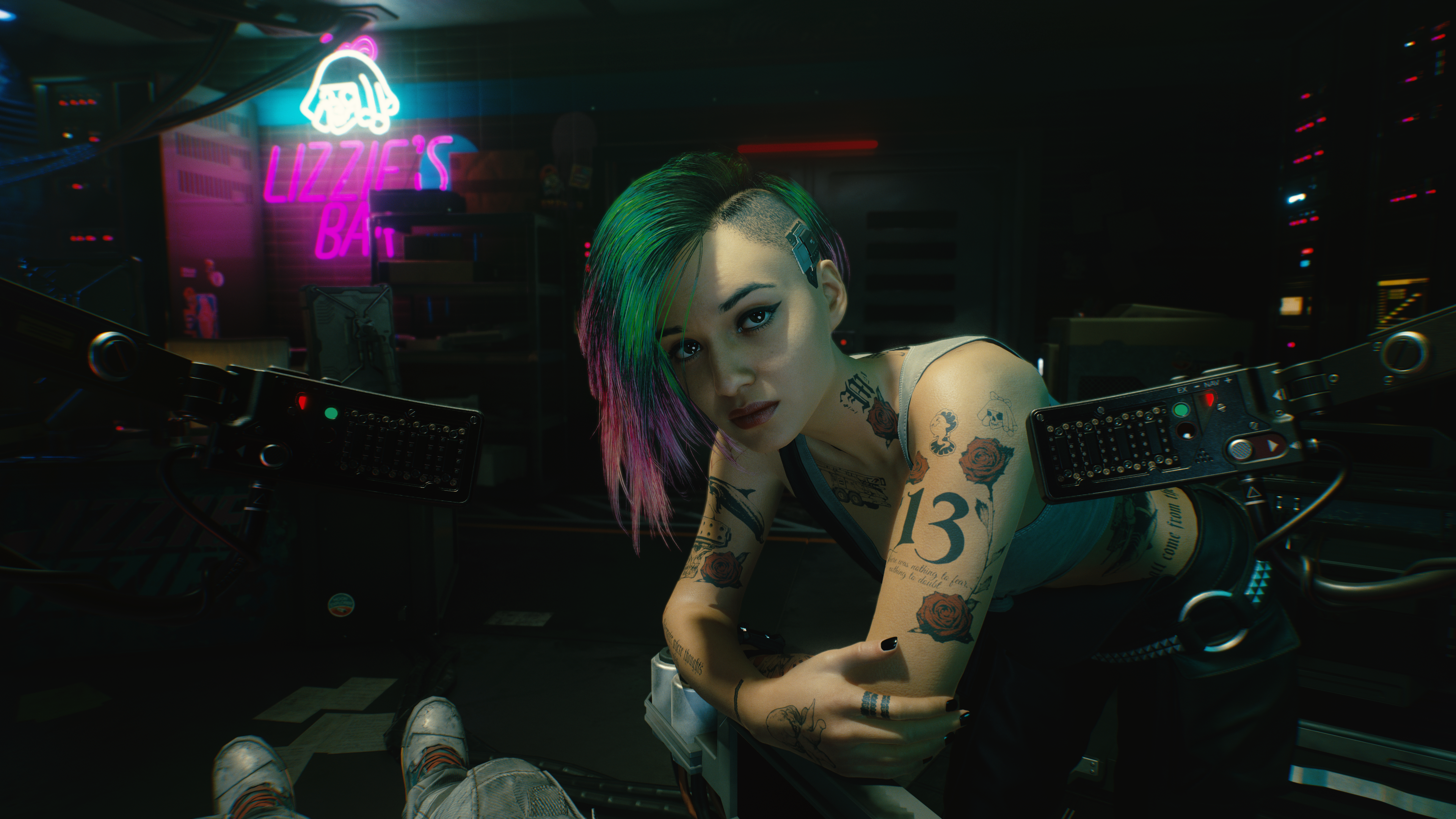 Una mujer con tatuajes y pelo teñido de verde mira a la cámara en una habitación oscura.
