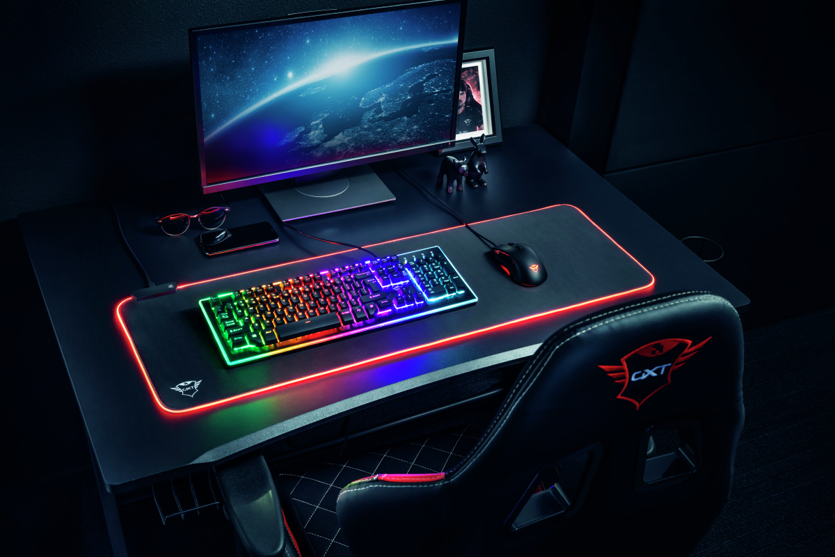 Configuración de juego con teclado, ratón y silla iluminados. Habitación oscura, vista superior.