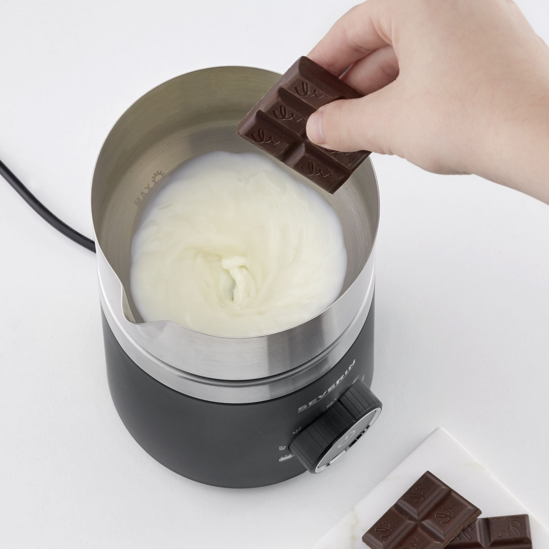 A hand pouring a chocolate bar into a milk frother.