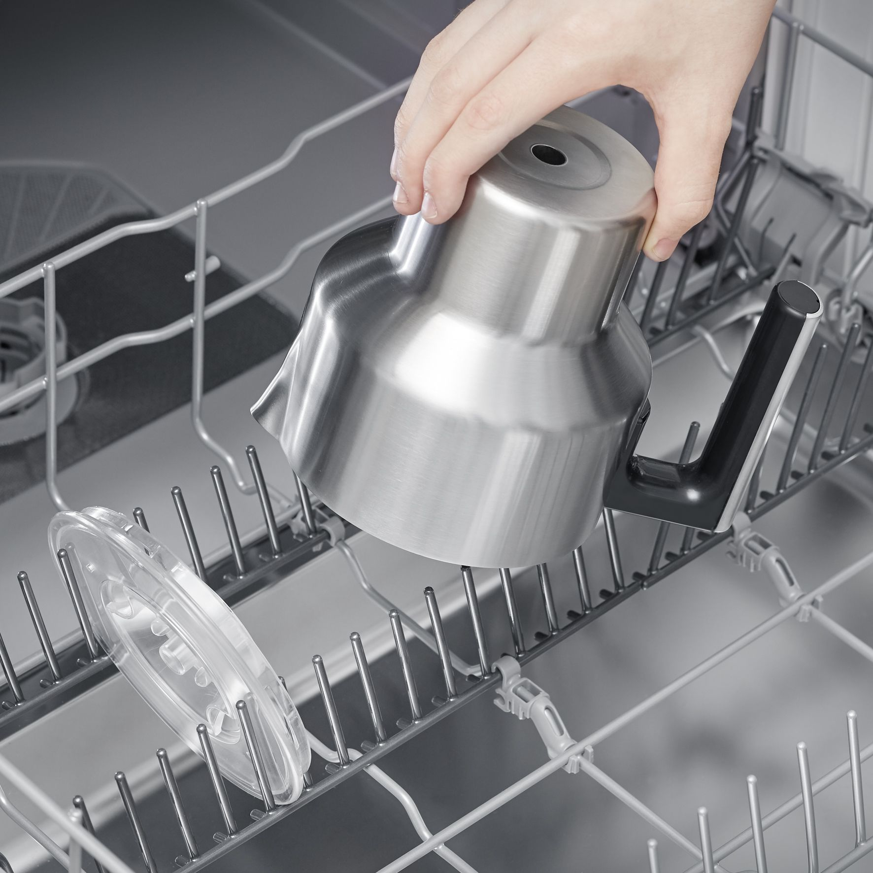 A hand is putting a stainless steel part of a kitchen appliance into a dishwasher.