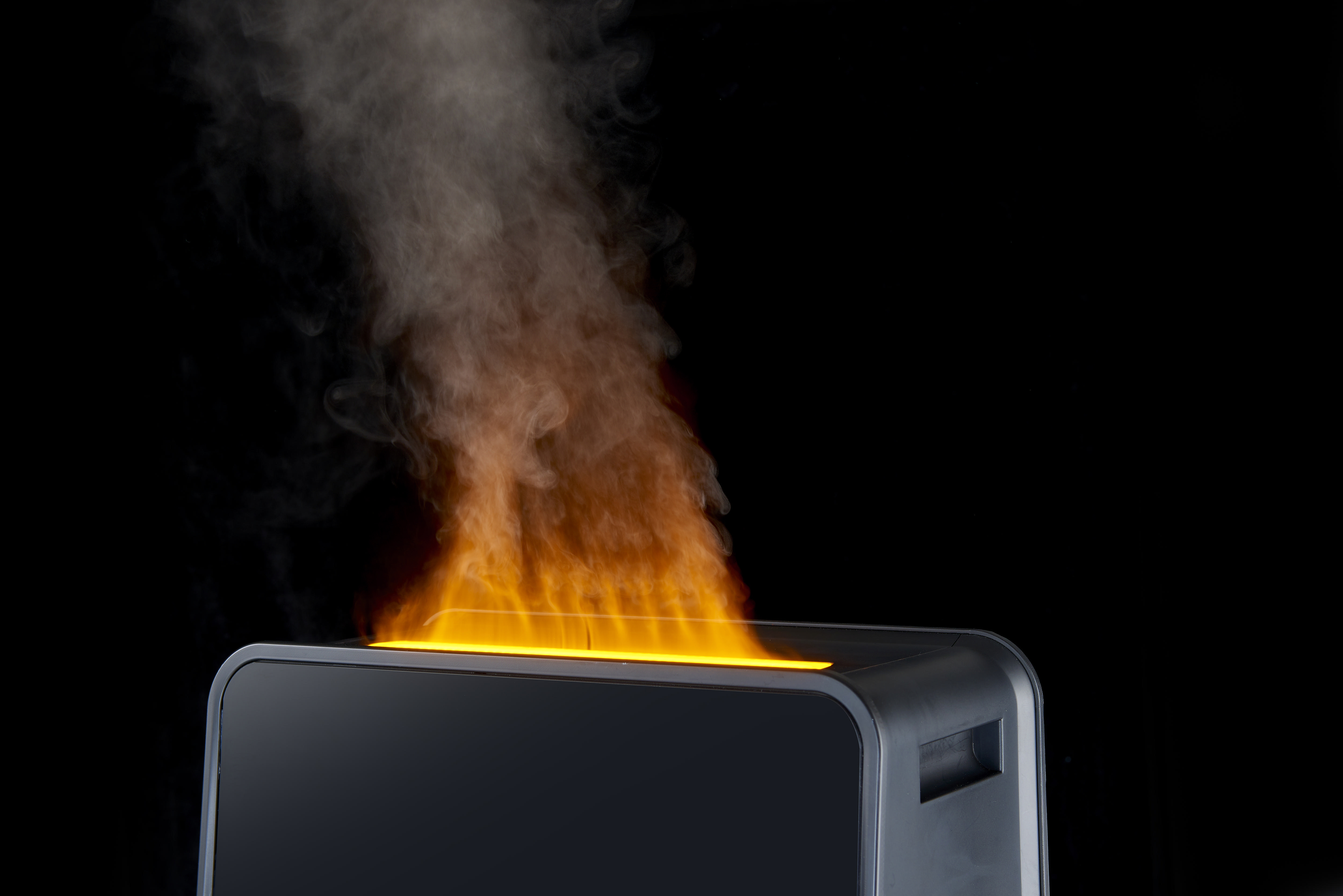 Ein schwarzes Gerät stößt orangefarbene Flammen und weißen Rauch aus.