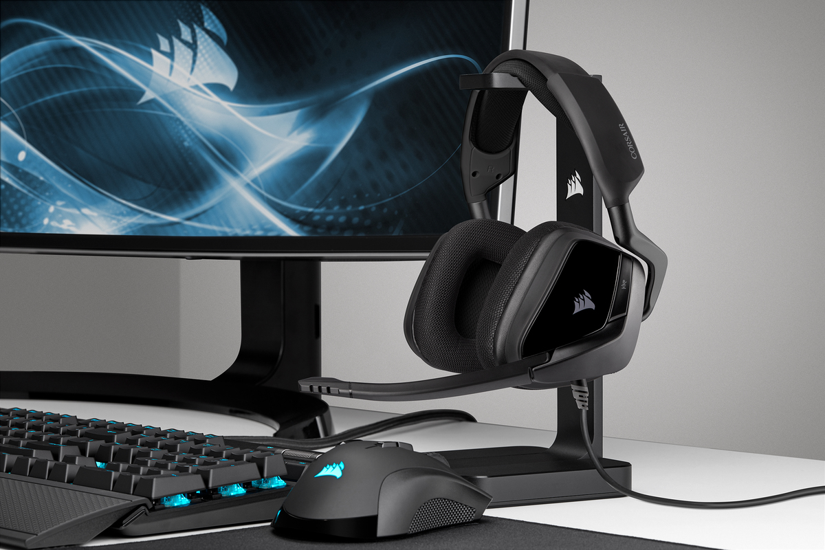 Auriculares gaming Corsair en un soporte con ratón y teclado en primer plano.