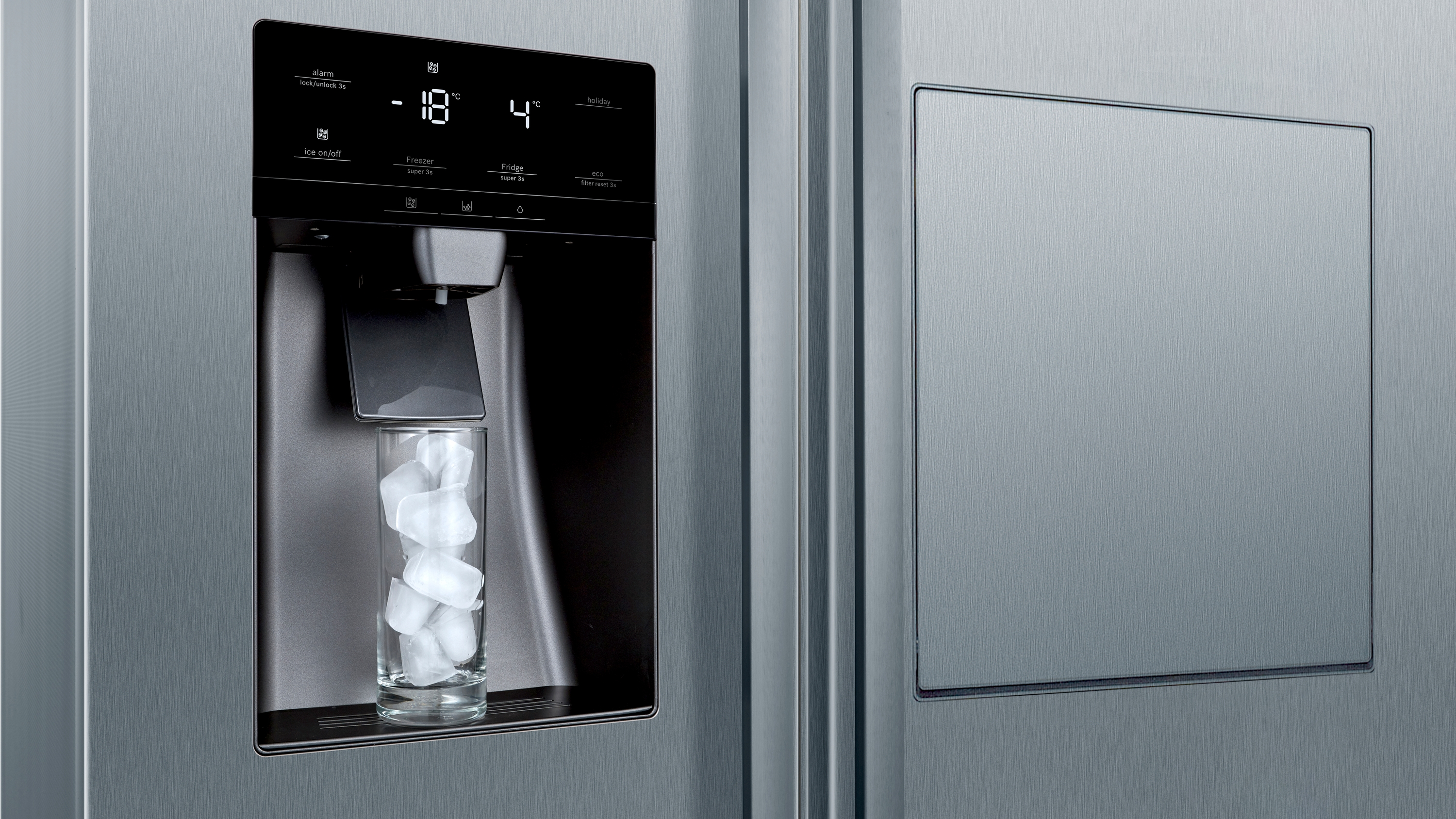 Nahaufnahme des Eis- und Wasserspenders eines Kühlschranks aus Edelstahl mit einem Glas Eis.