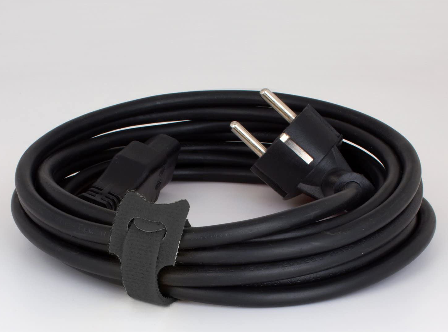 Cordon d'alimentation noir. Prise et connecteur à chaque extrémité, enroulés et maintenus par une sangle.