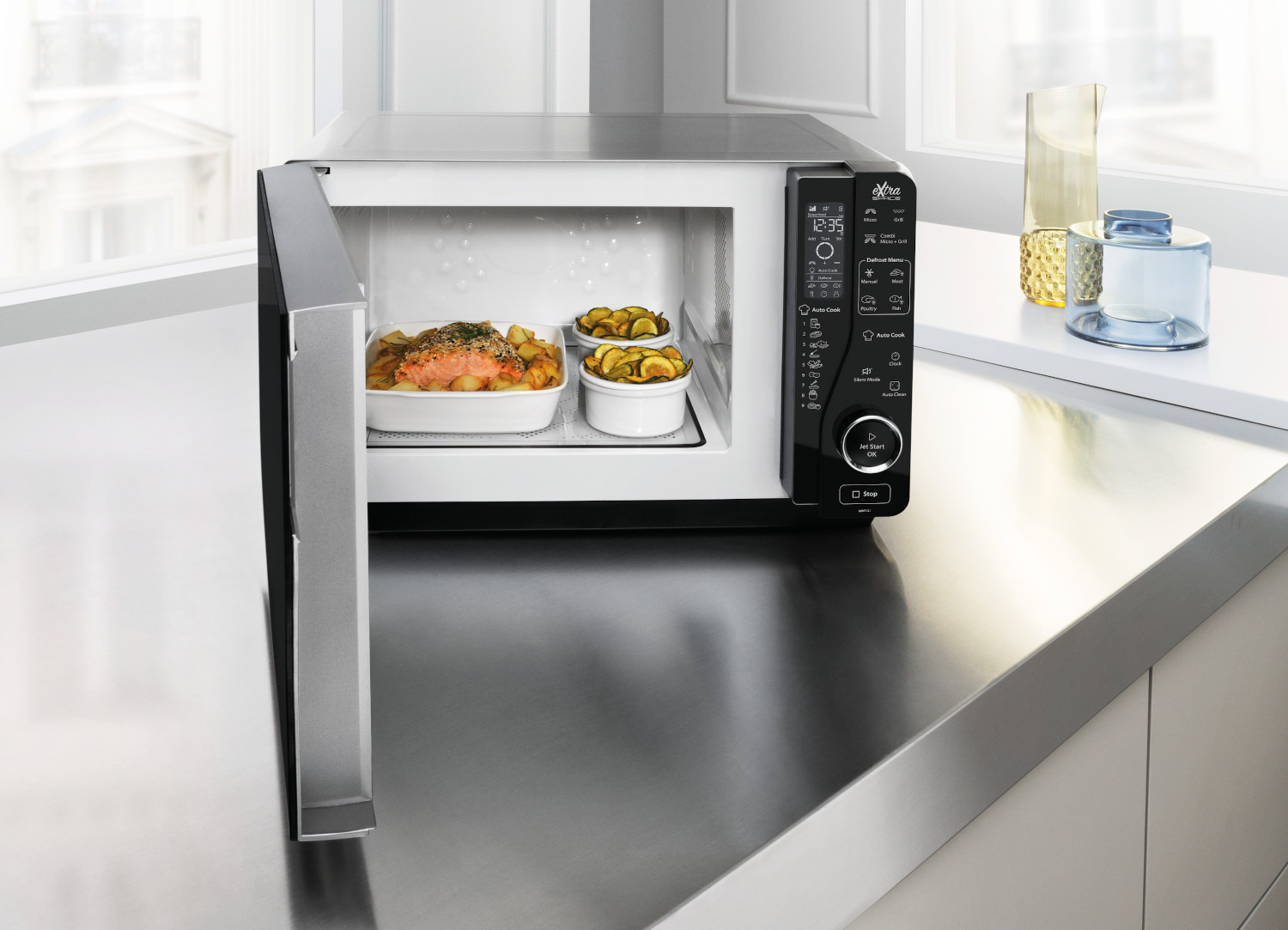 Microwave oven with open door, two dishes inside, on a stainless steel countertop.
