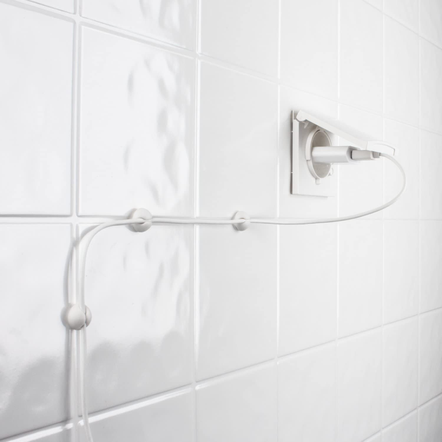 Un muro bianco con piastrelle bianche ha una presa di corrente con un cavo collegato.