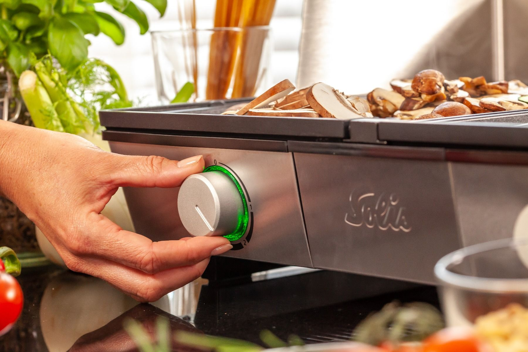 Een hand die een zilveren knop op een grill afstelt. De knop is omgeven door groen licht.