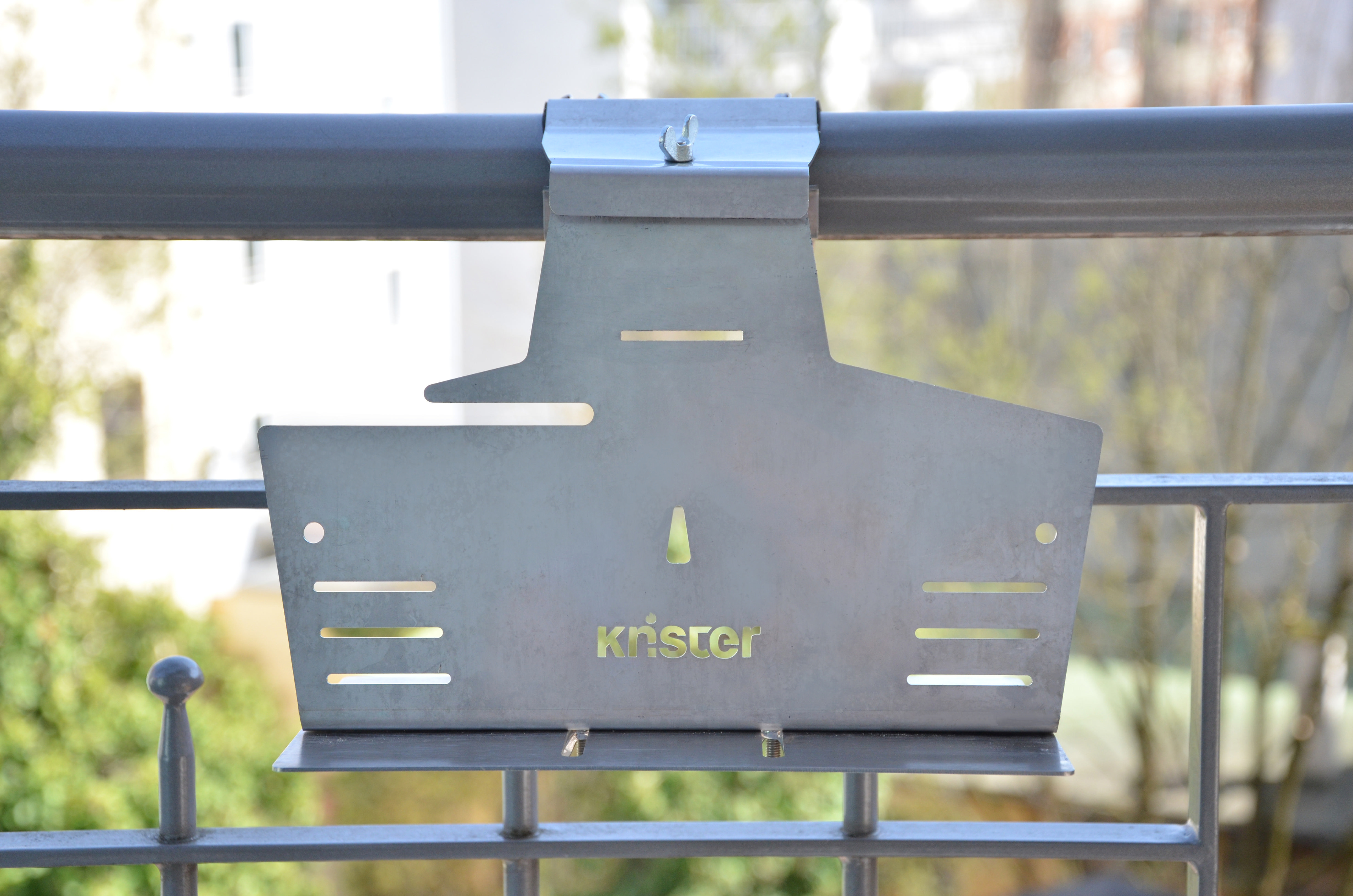 Metall-Balkon-Pflanzenhalterung, an einem Geländer befestigt, Außenbereich mit grünen Pflanzen.