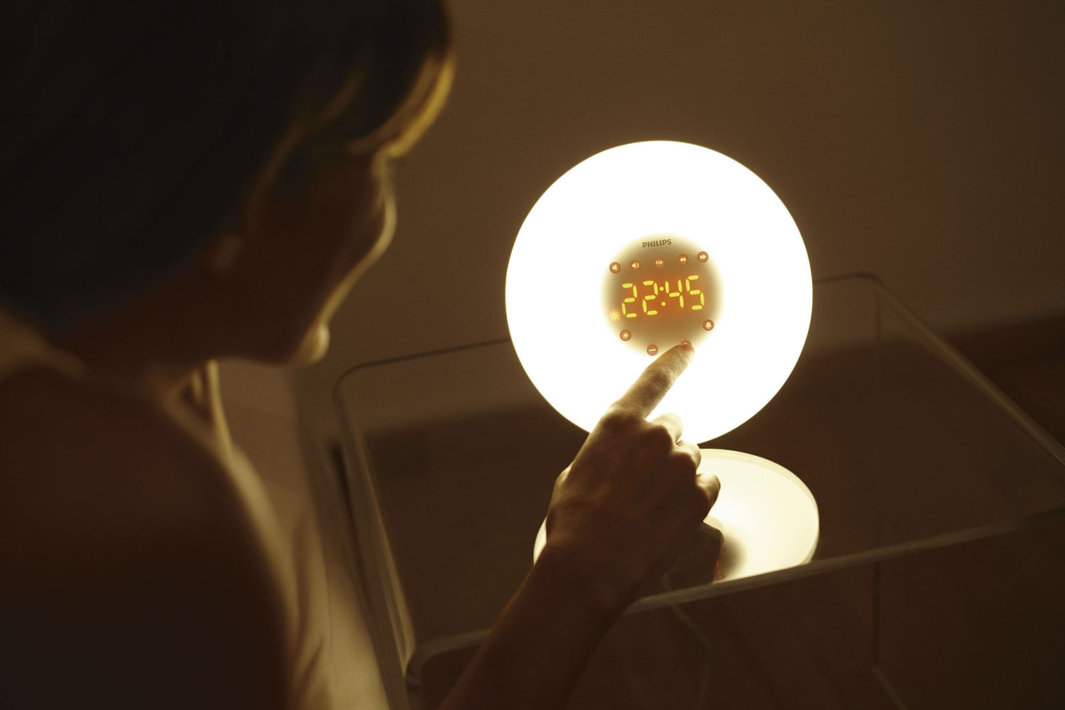 De hand van een vrouw raakt een oplichtende witte Philips-klok aan, die de tijd weergeeft.